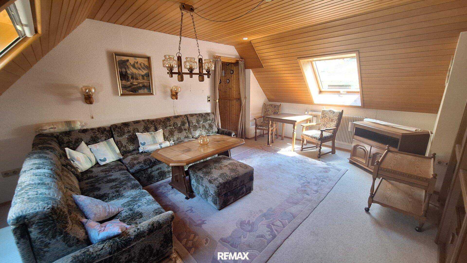 Gemütliches Wohnzimmer im Dachgeschoss mit Schrägdach, Holztäfelung und großer Eckcouch.