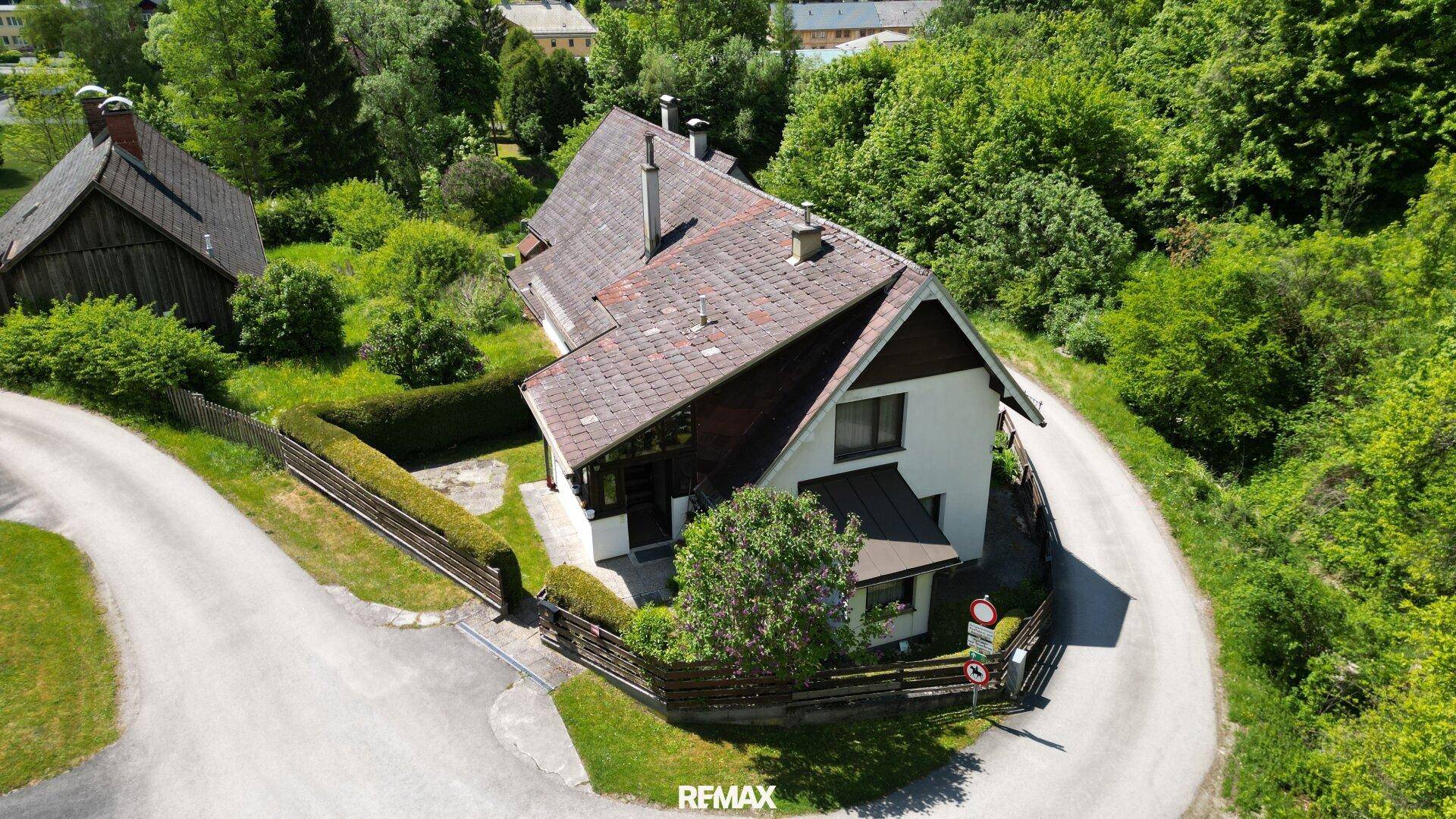 Luftaufnahme eines Hauses an einer Kurve, umgeben von Bäumen und einem gepflegten Garten.