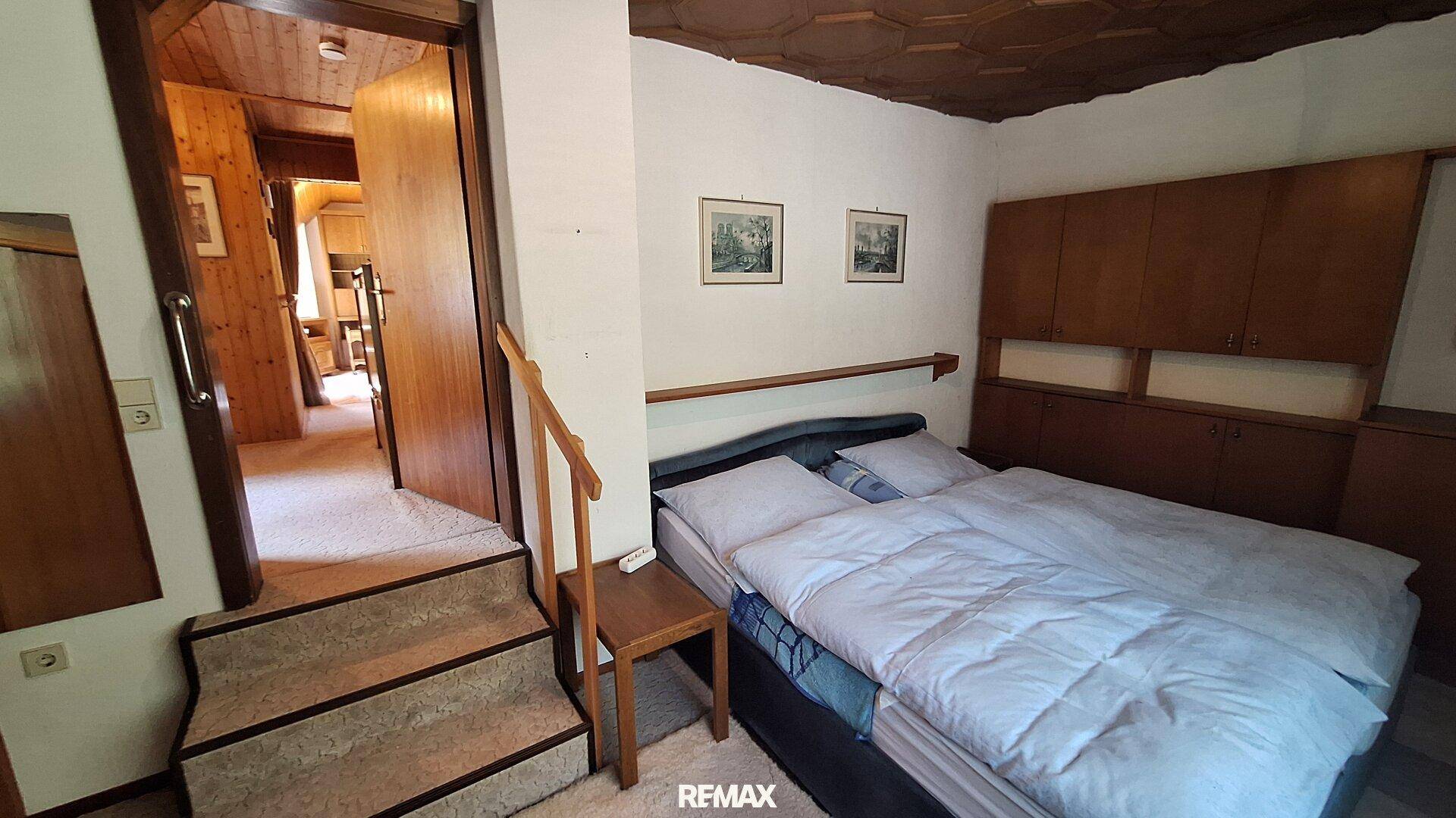 Schlafzimmer mit Doppelbett, Holzmöbeln und Zugang zu einem weiteren Raum.