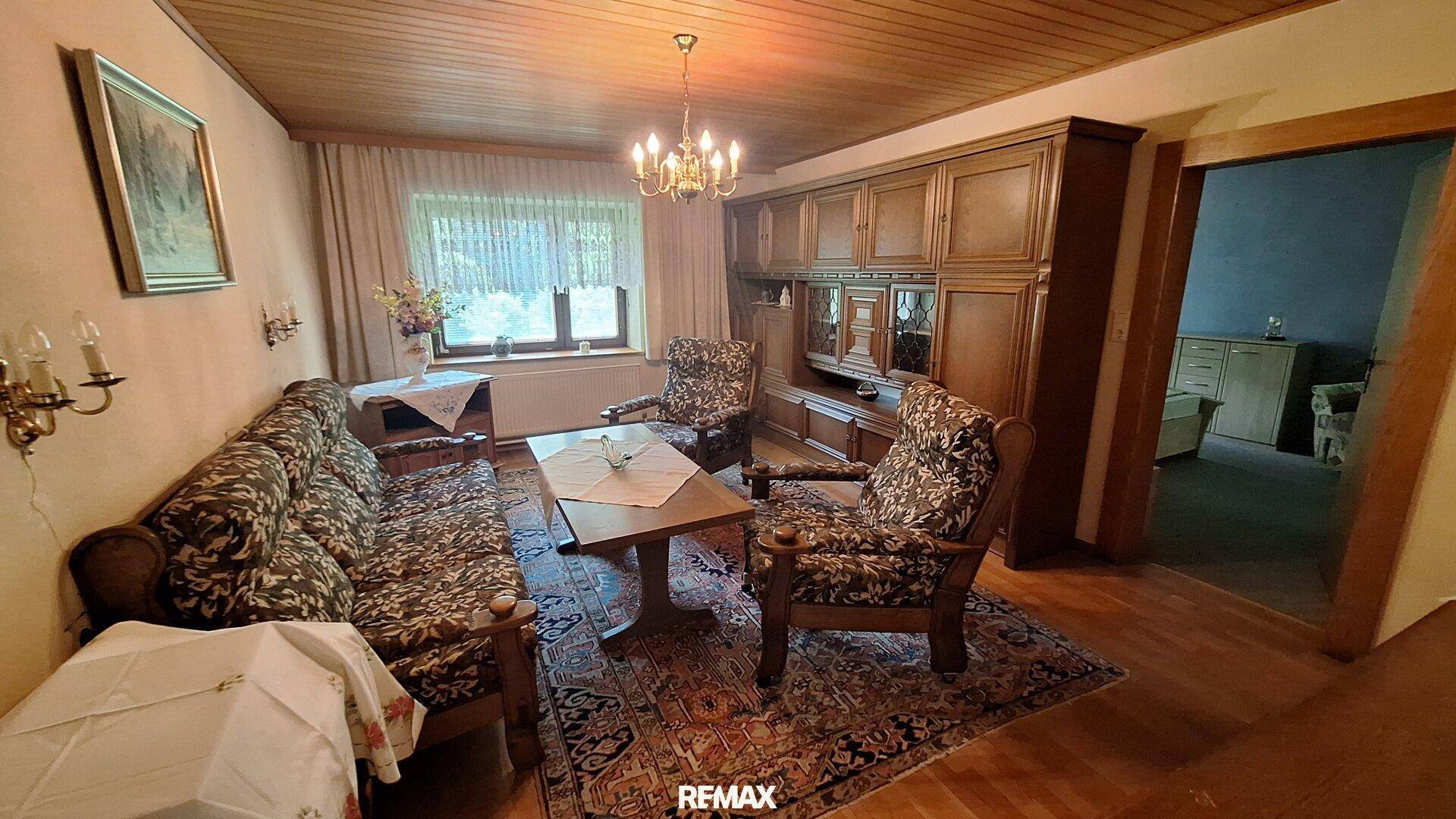 Traditionelles Wohnzimmer mit dunklen Holzmöbeln, gemustertem Teppich und großem Fenster.
