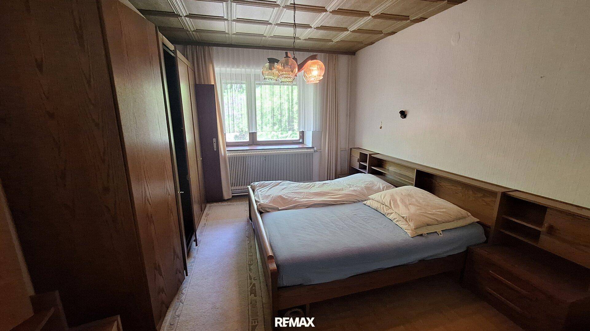 Schlafzimmer mit zwei Einzelbetten, Holzschrank und Fenster mit Blick ins Grüne.