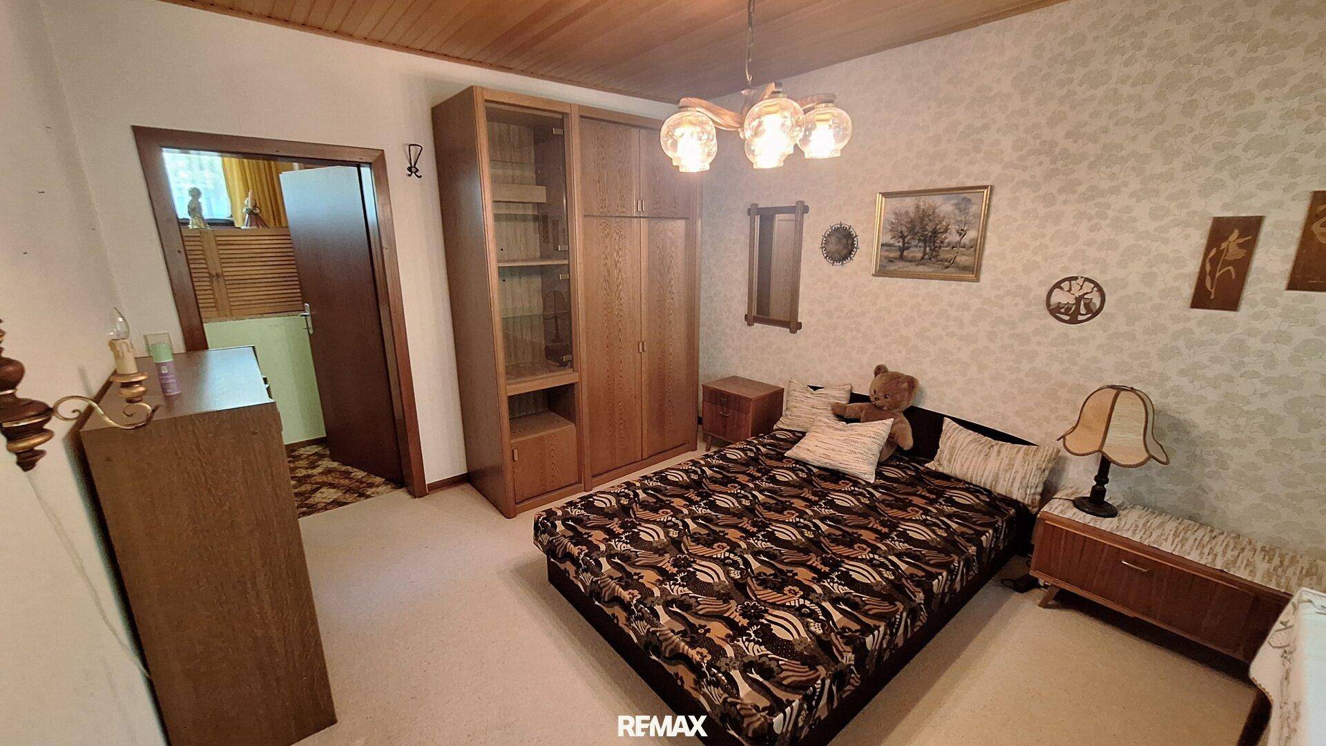 Schlafzimmer mit Doppelbett, Holzschrank und gemusterter Tapete.