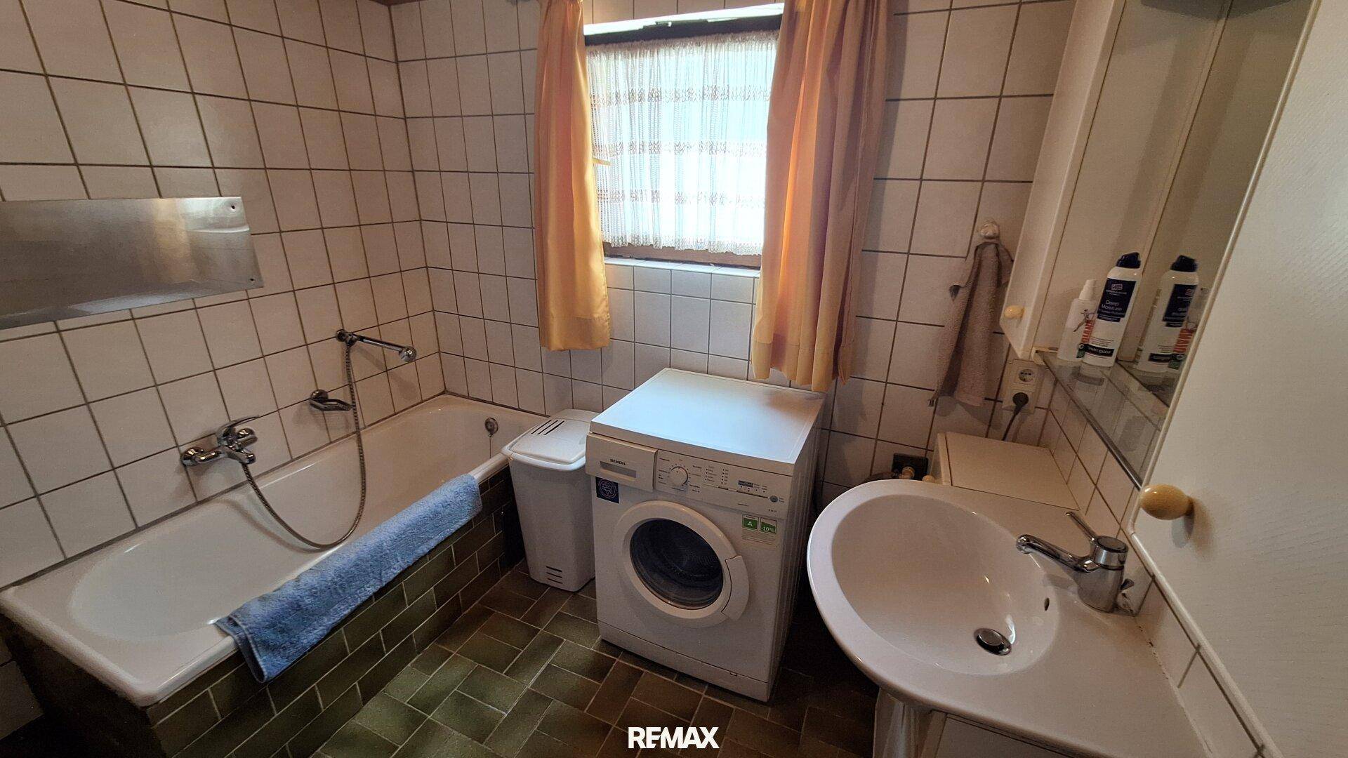 Badezimmer mit Badewanne, Waschmaschine und Fliesenboden in Grün- und Weißtönen.