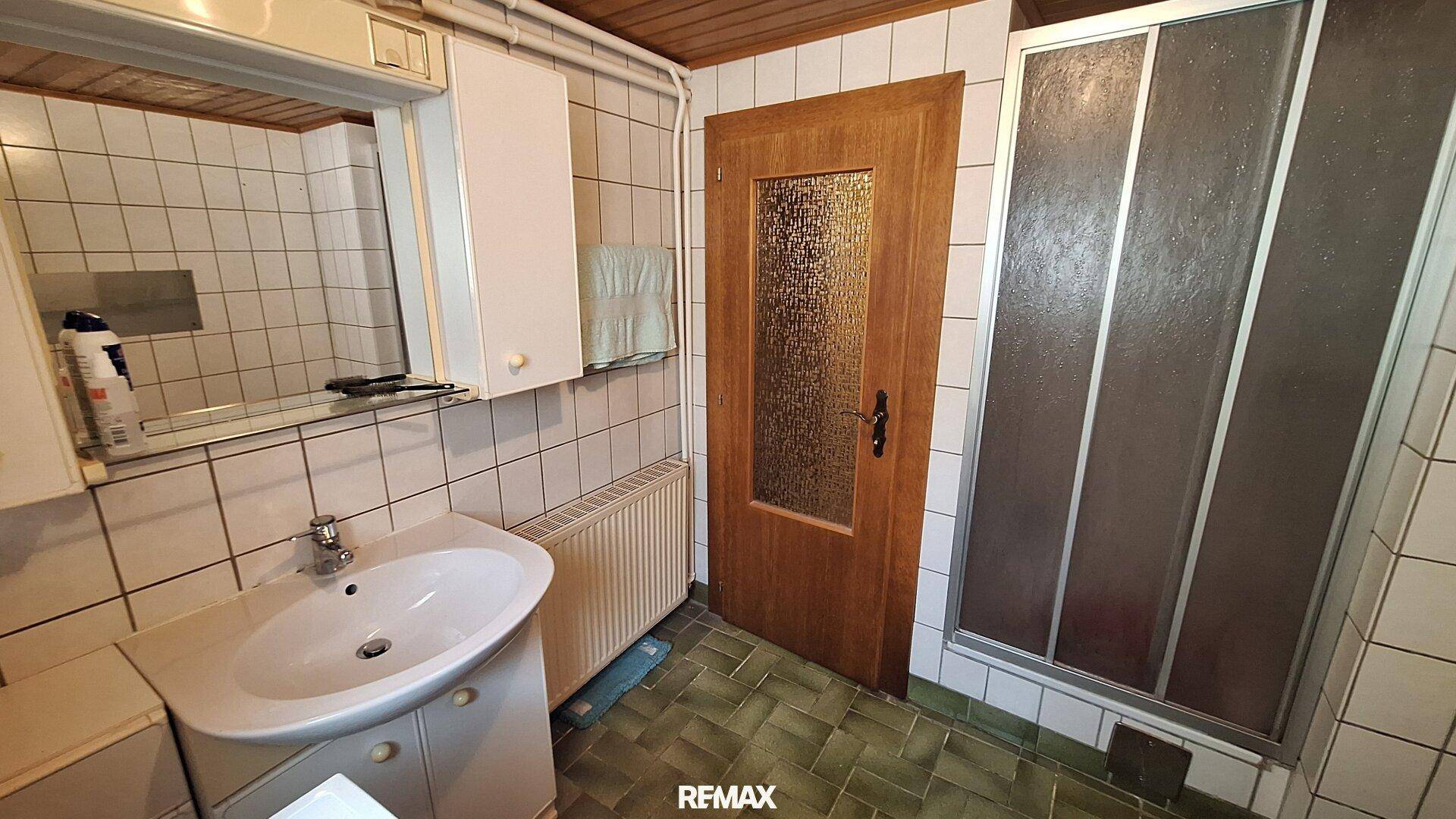 Badezimmer mit Dusche, Waschbecken und Fliesen in Grün- und Weißtönen.