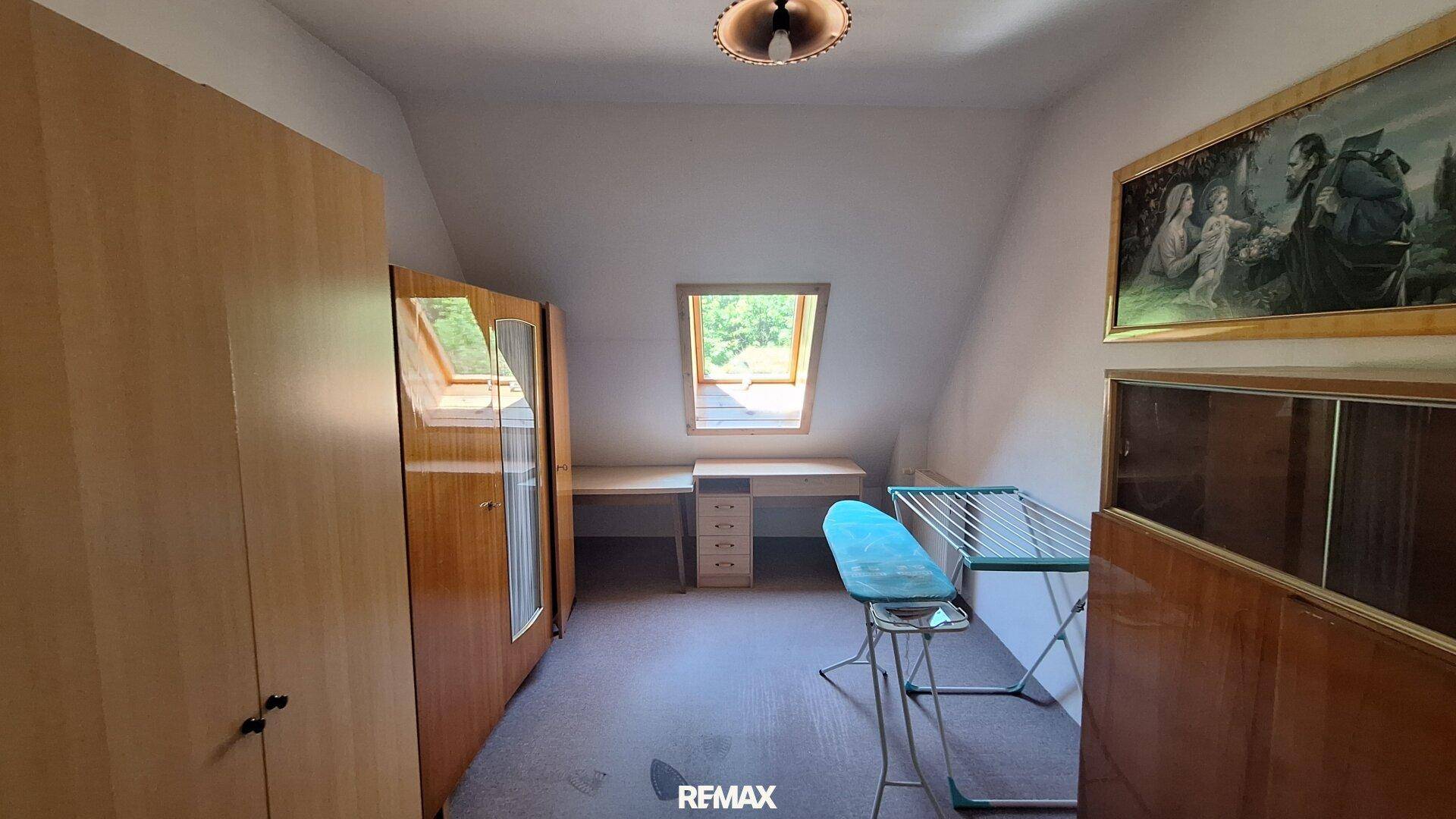 Dachgeschosszimmer mit Schrägdach, Dachfenster und Schreibtischbereich.