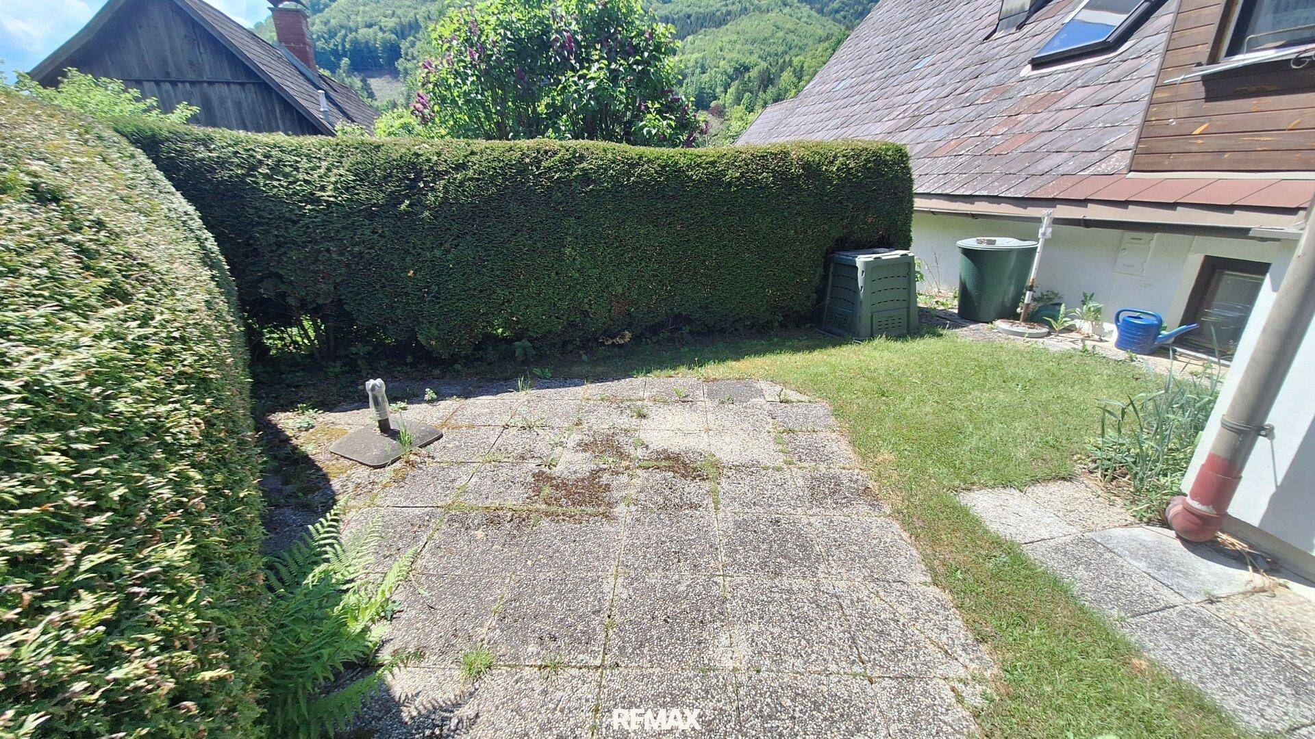 Kleiner Gartenbereich mit gepflegter Hecke, Rasenfläche und einer einfachen gepflasterten Terrasse.