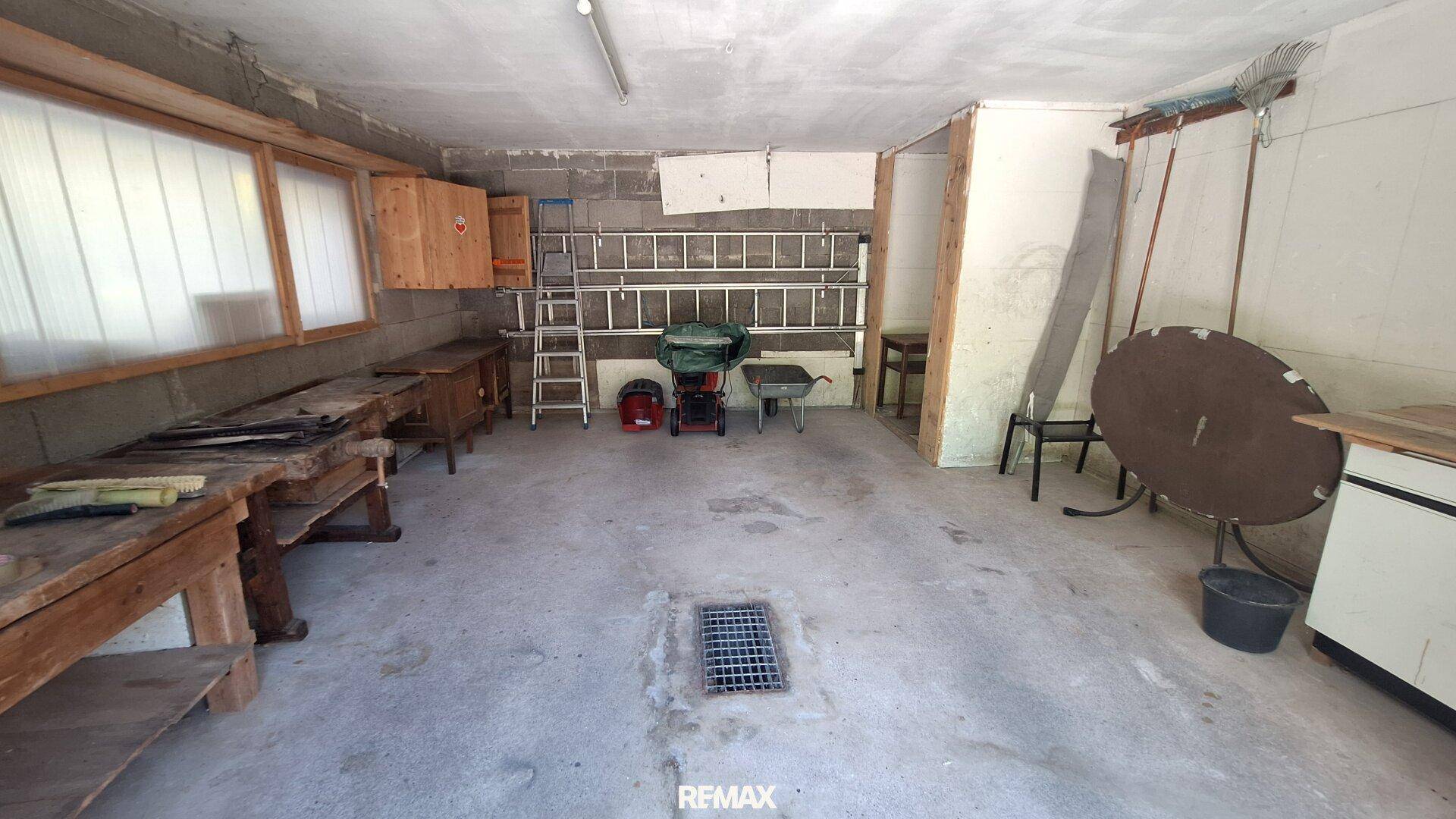 Geräumige Werkstatt oder Garage mit Betonboden, Werkbänken und verschiedenen Geräten.