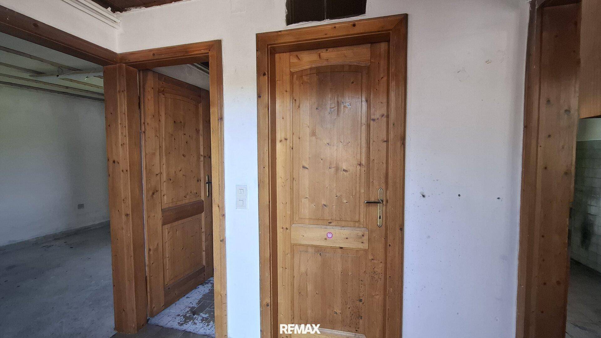 Flur mit zwei rustikalen Holztüren und weiß gestrichenen Wänden in einem älteren Gebäude.