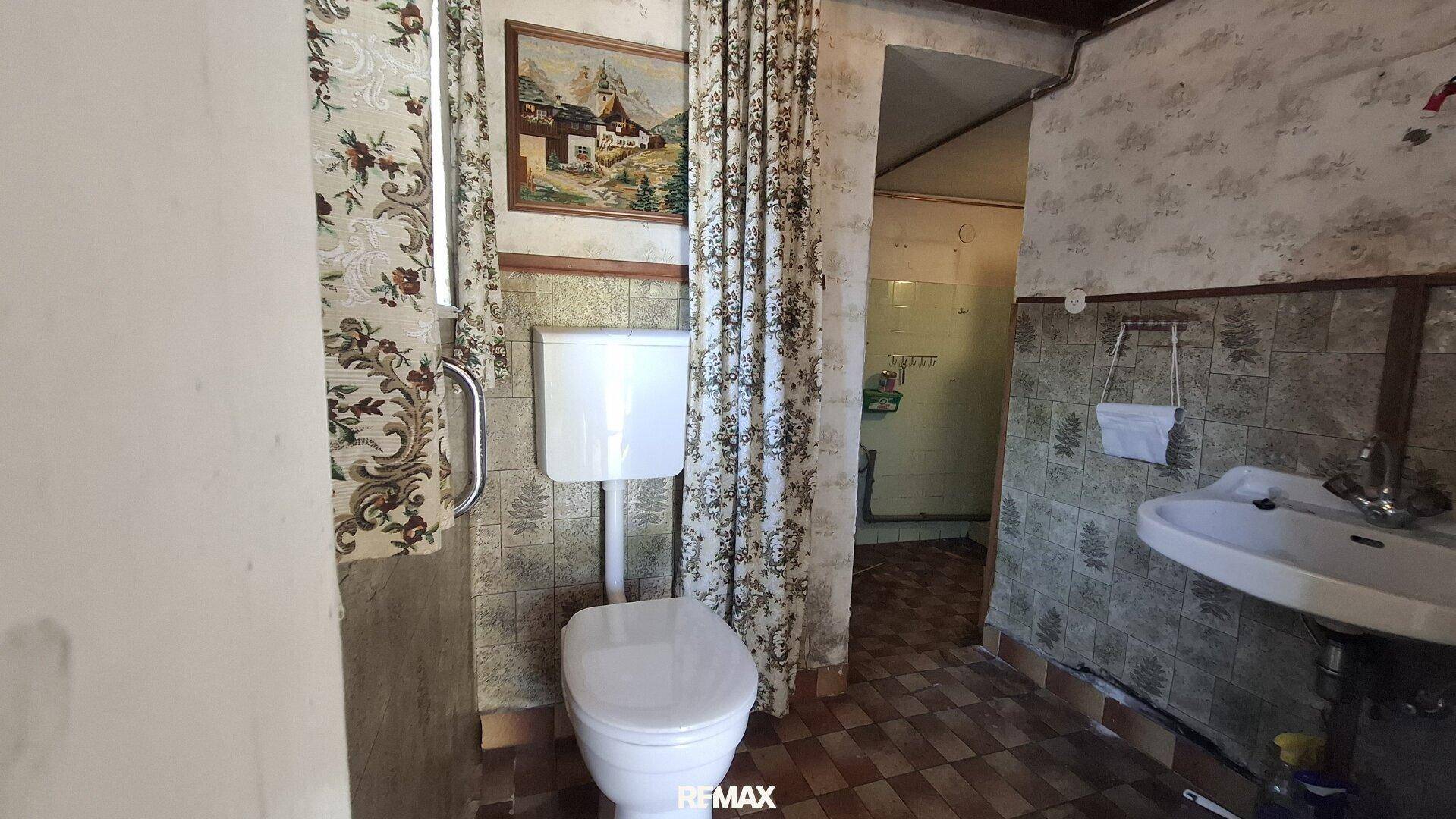Einfaches WC mit gemusterten Fliesen, Toilette und kleinem Waschbecken in älterem Stil.
