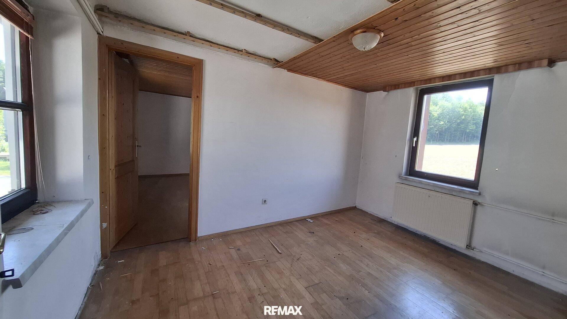 Helles Schlafzimmer mit Holzdielenboden, Holzdecke und zwei Fenstern mit Blick ins Grüne.