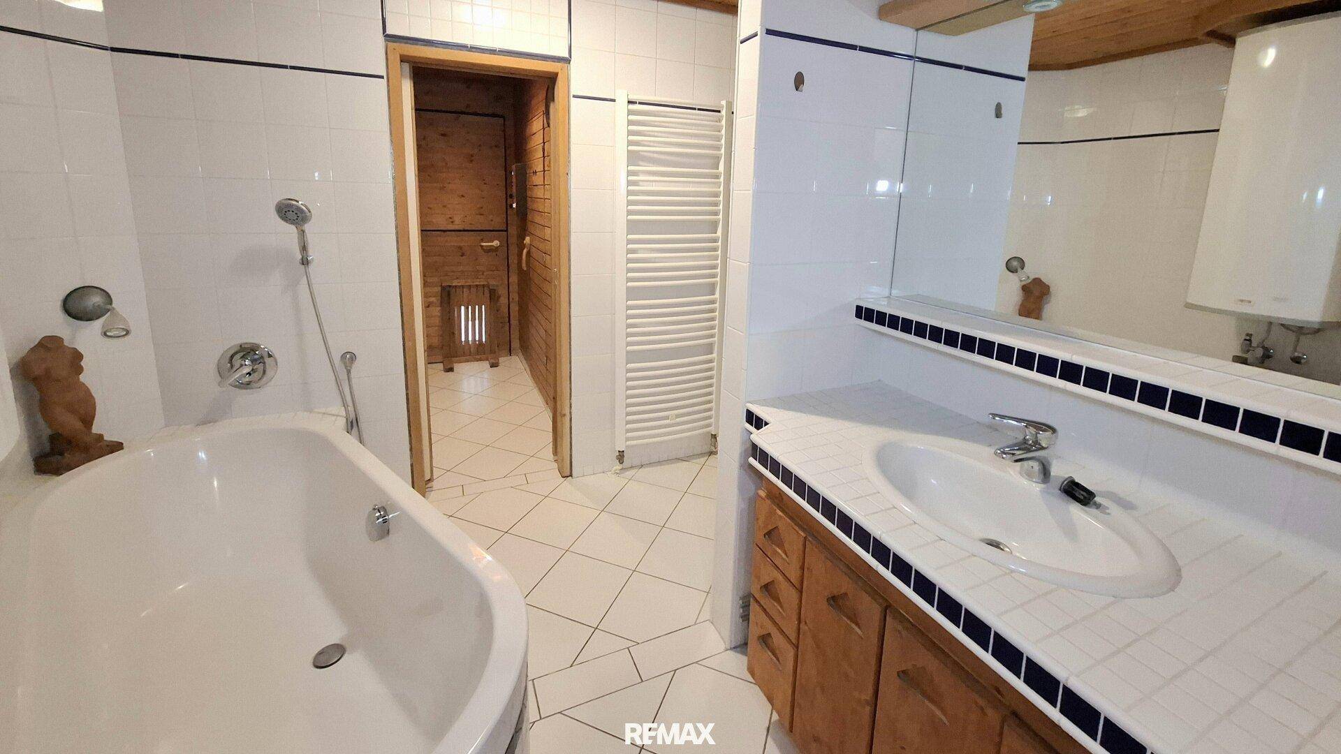 Badezimmer mit Badewanne, Waschbecken und direktem Zugang zu einer holzvertäfelten Sauna.