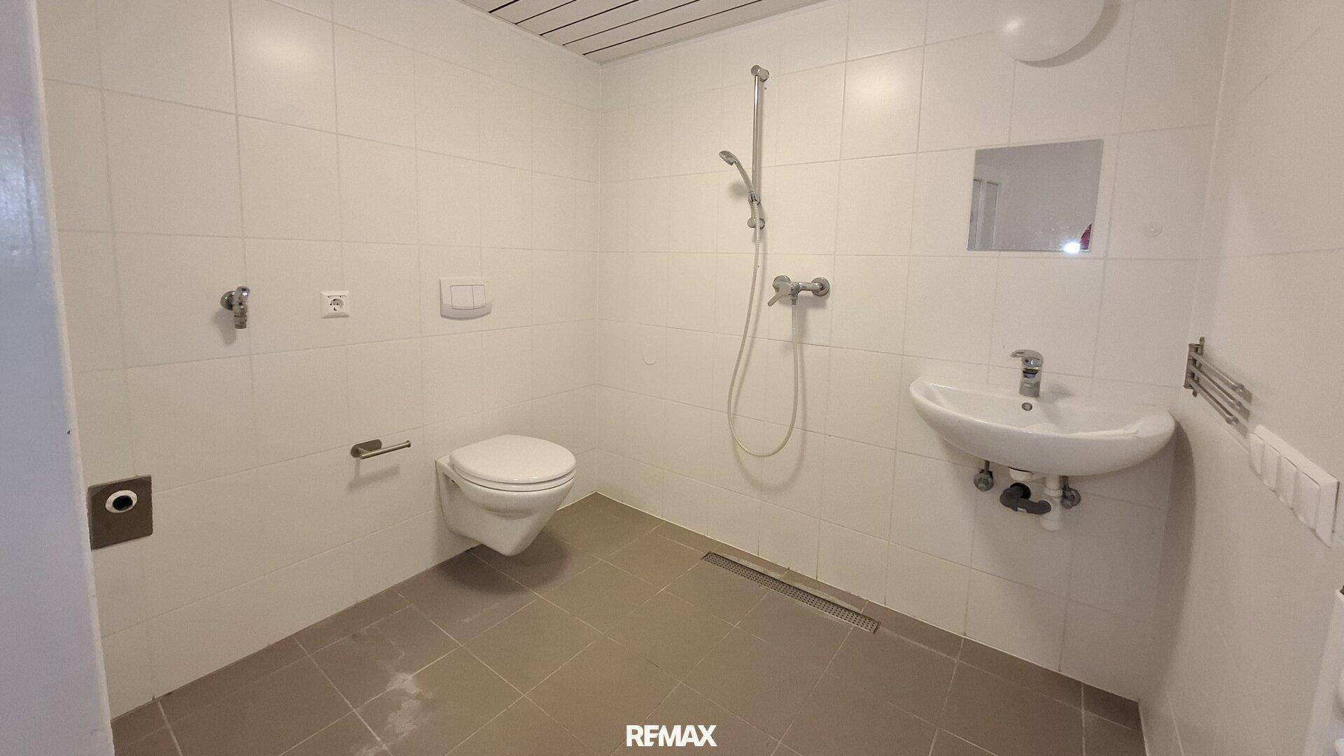 Modern gefliestes Badezimmer mit Dusche, wandhängendem WC und Waschbecken.