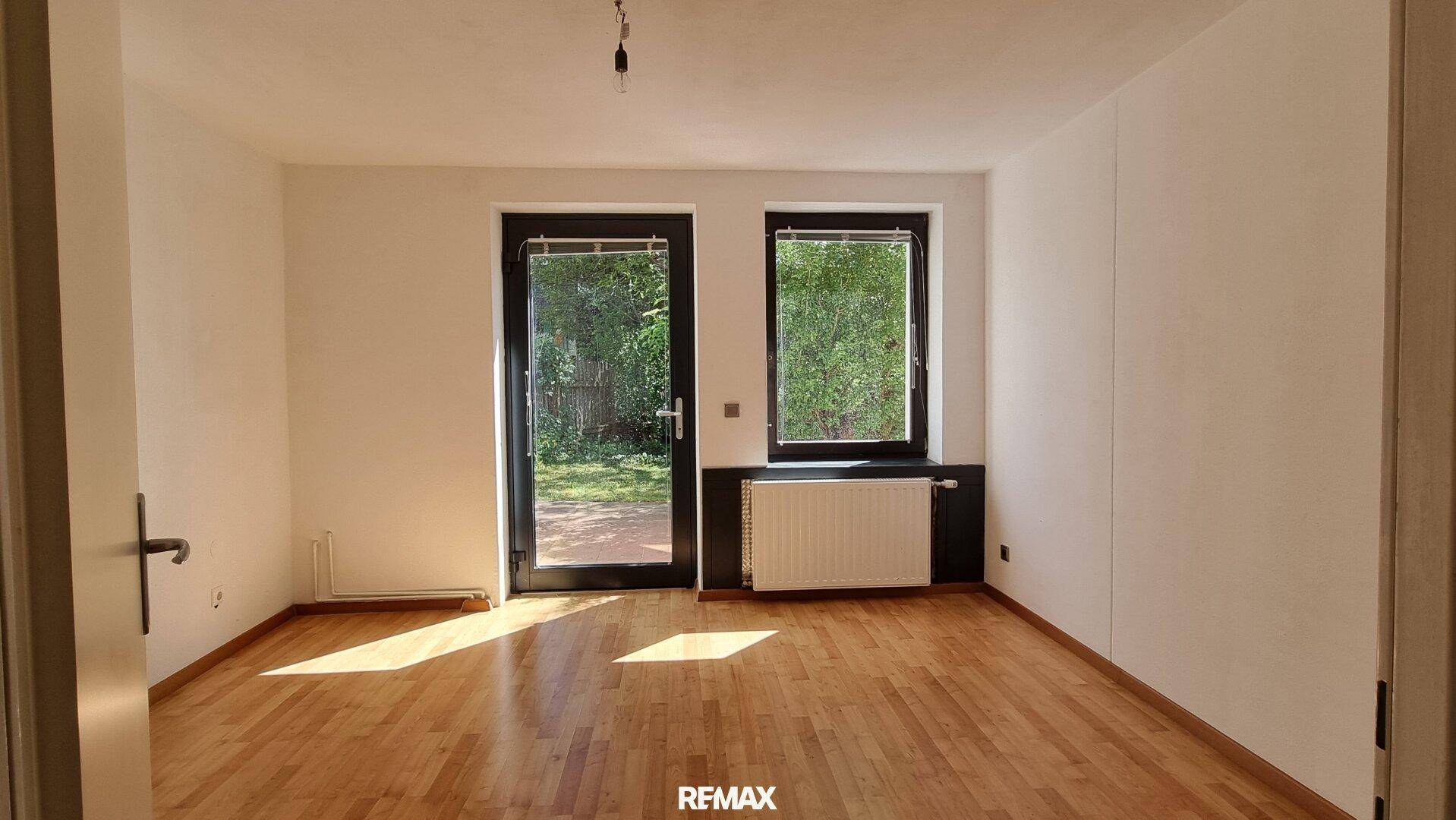 Helles Wohnzimmer mit Parkettboden und großen Fenstern, die Zugang zum Garten bieten.