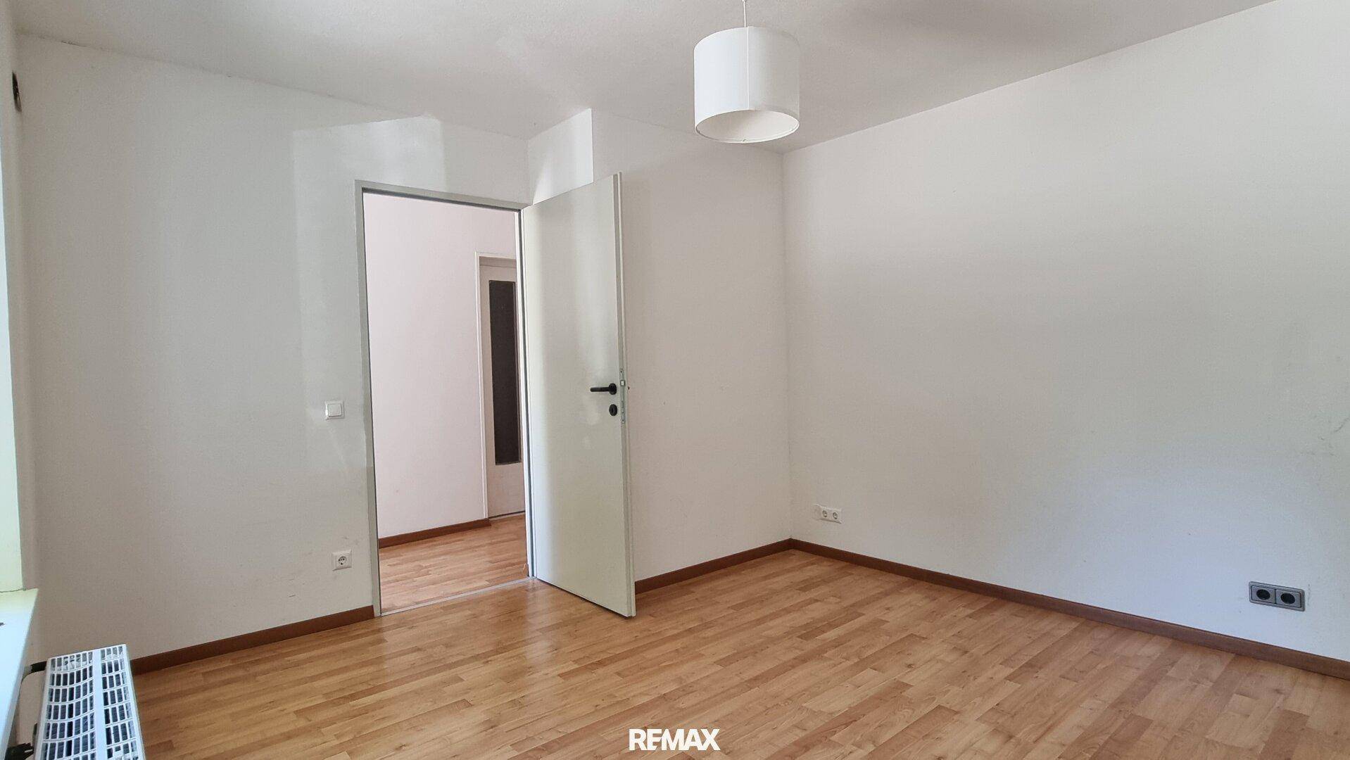 Schlafzimmer mit hellem Parkettboden und offener Tür zu einem angrenzenden Raum.