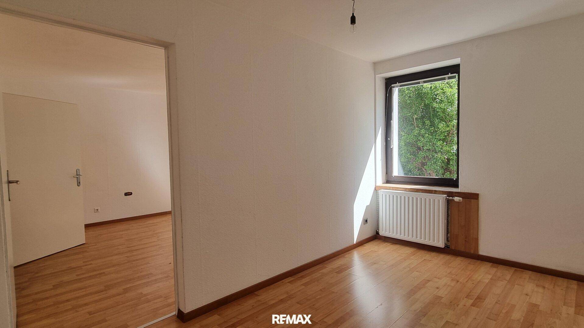 Helles Schlafzimmer mit Parkettboden und Fenster mit Blick ins Grüne.