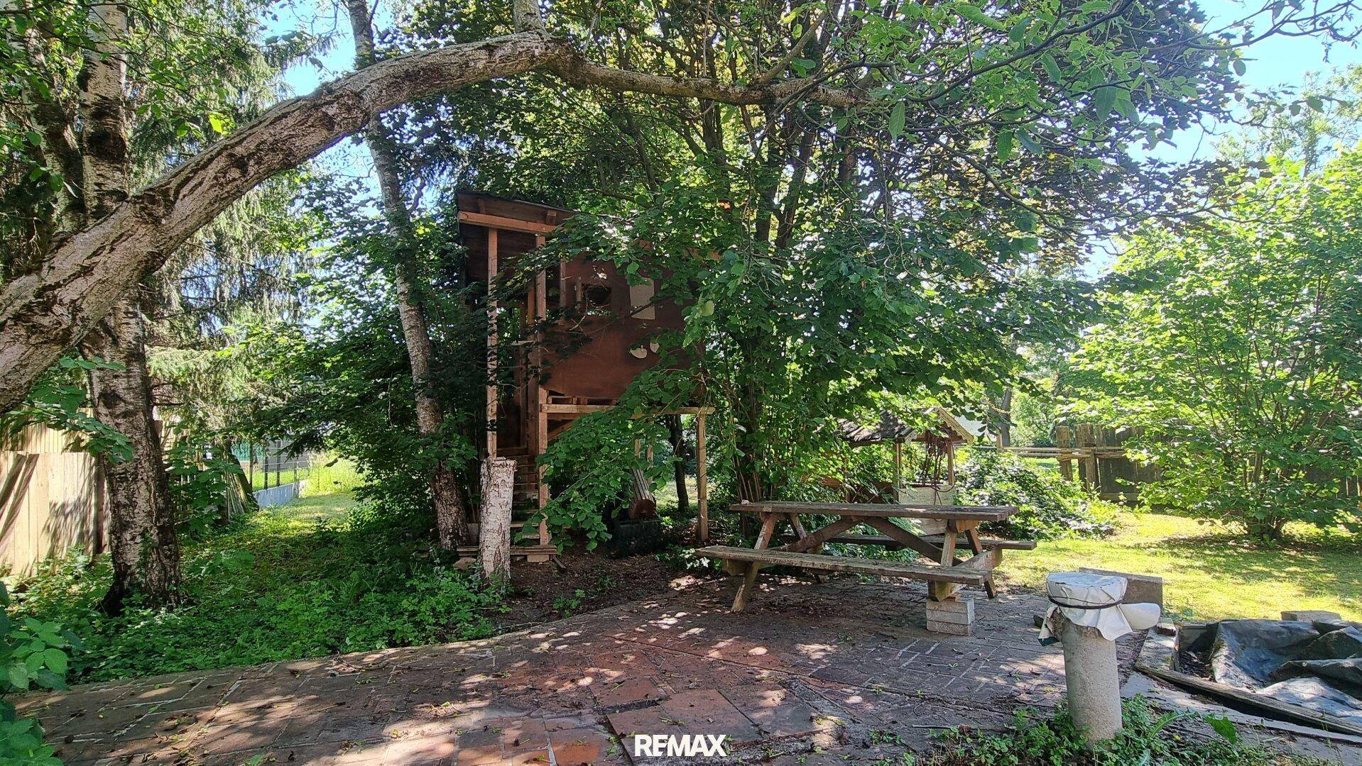 Naturbelassener Gartenbereich mit Baumhaus, Picknicktisch und viel Grün.