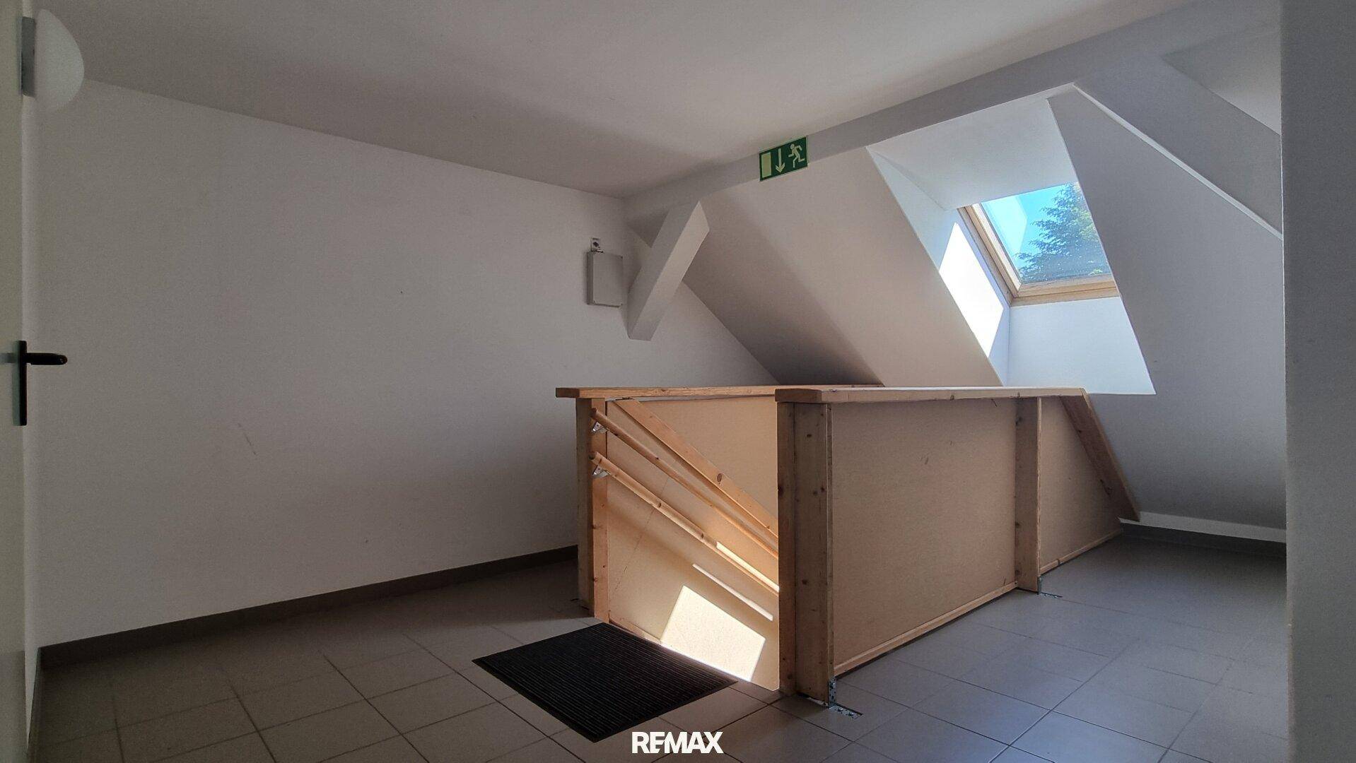 Heller Treppenabsatz im Dachgeschoss mit Dachfenster und Holzgeländer.