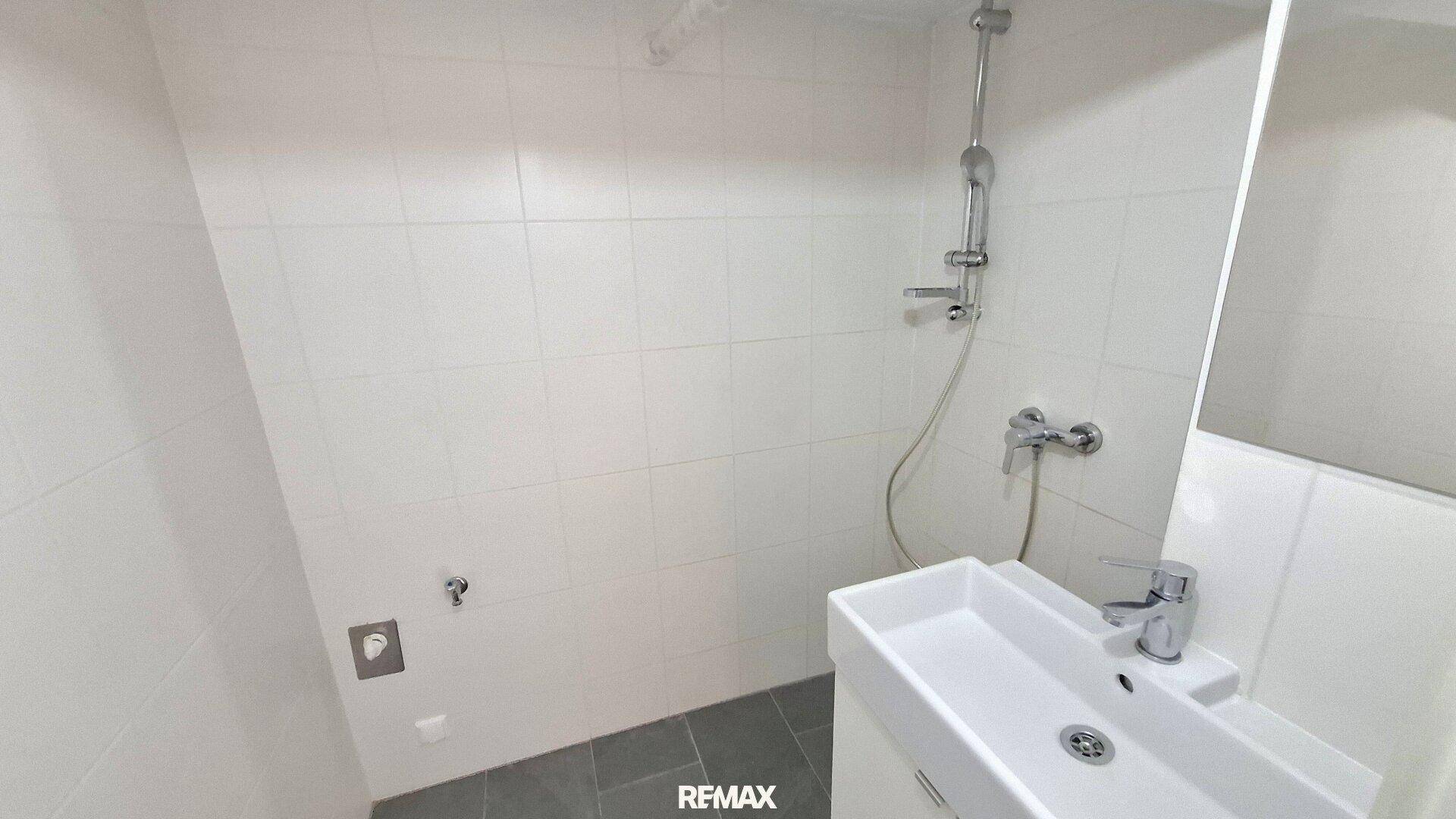 Modernes Badezimmer mit weiß gefliesten Wänden, Dusche und rechteckigem Waschbecken.