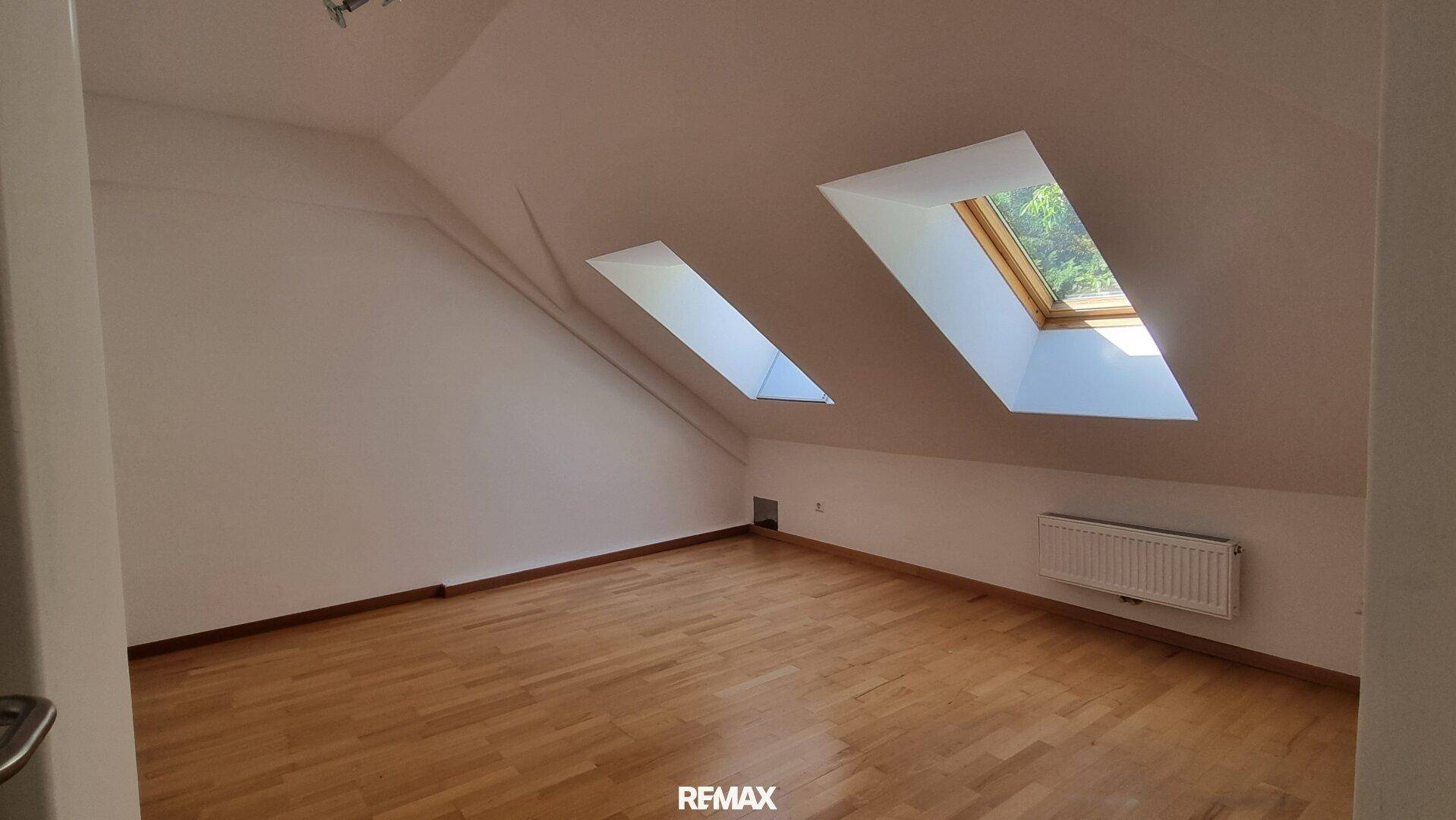 Helles Dachzimmer mit Holzboden und zwei Dachfenstern, ideal als Schlaf- oder Arbeitszimmer.