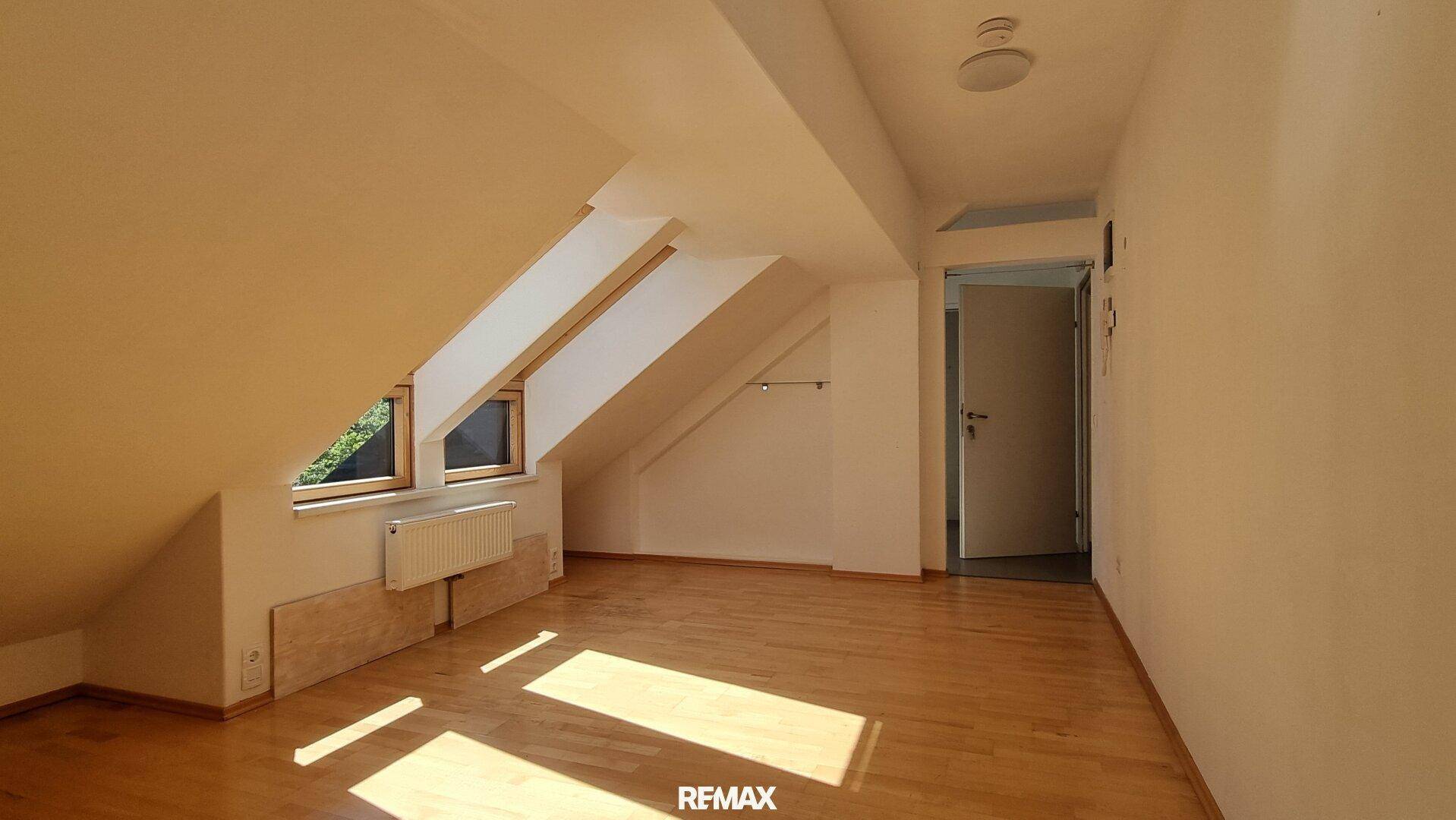 Helles Zimmer mit Holzboden und mehreren Fenstern, bietet viel Tageslicht.