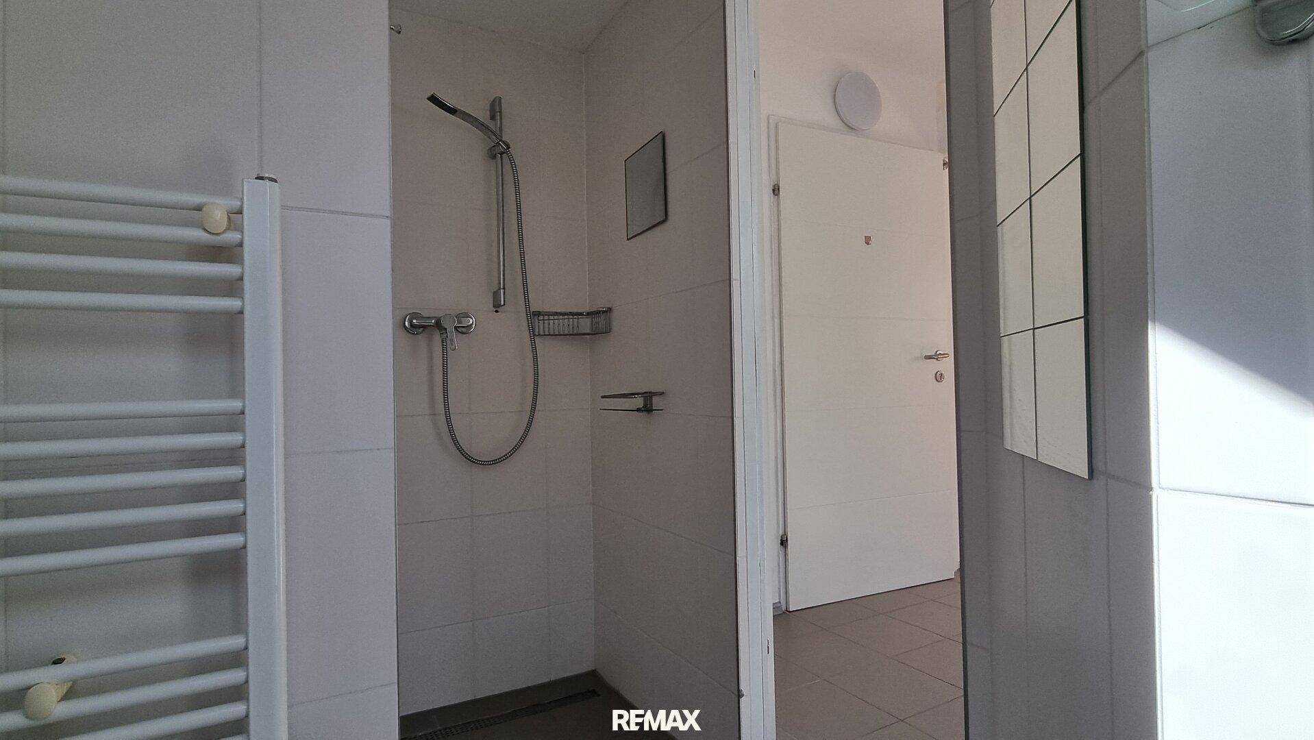 Duschbereich im Badezimmer mit weißen Fliesen und beheiztem Handtuchhalter.