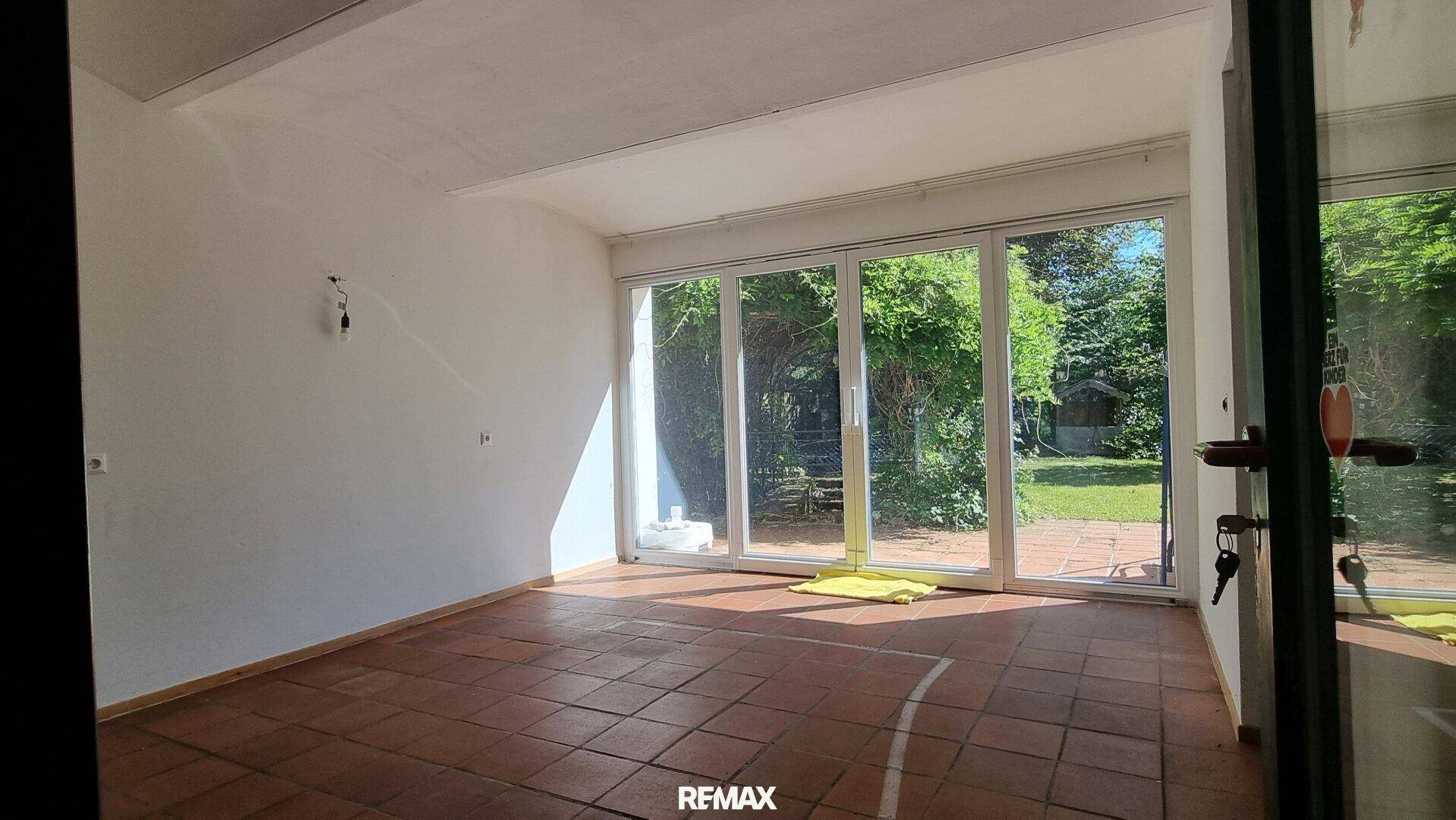 Heller Wohnraum mit großen Fenstern und Terrassentüren, die einen schönen Blick in den Garten bieten.