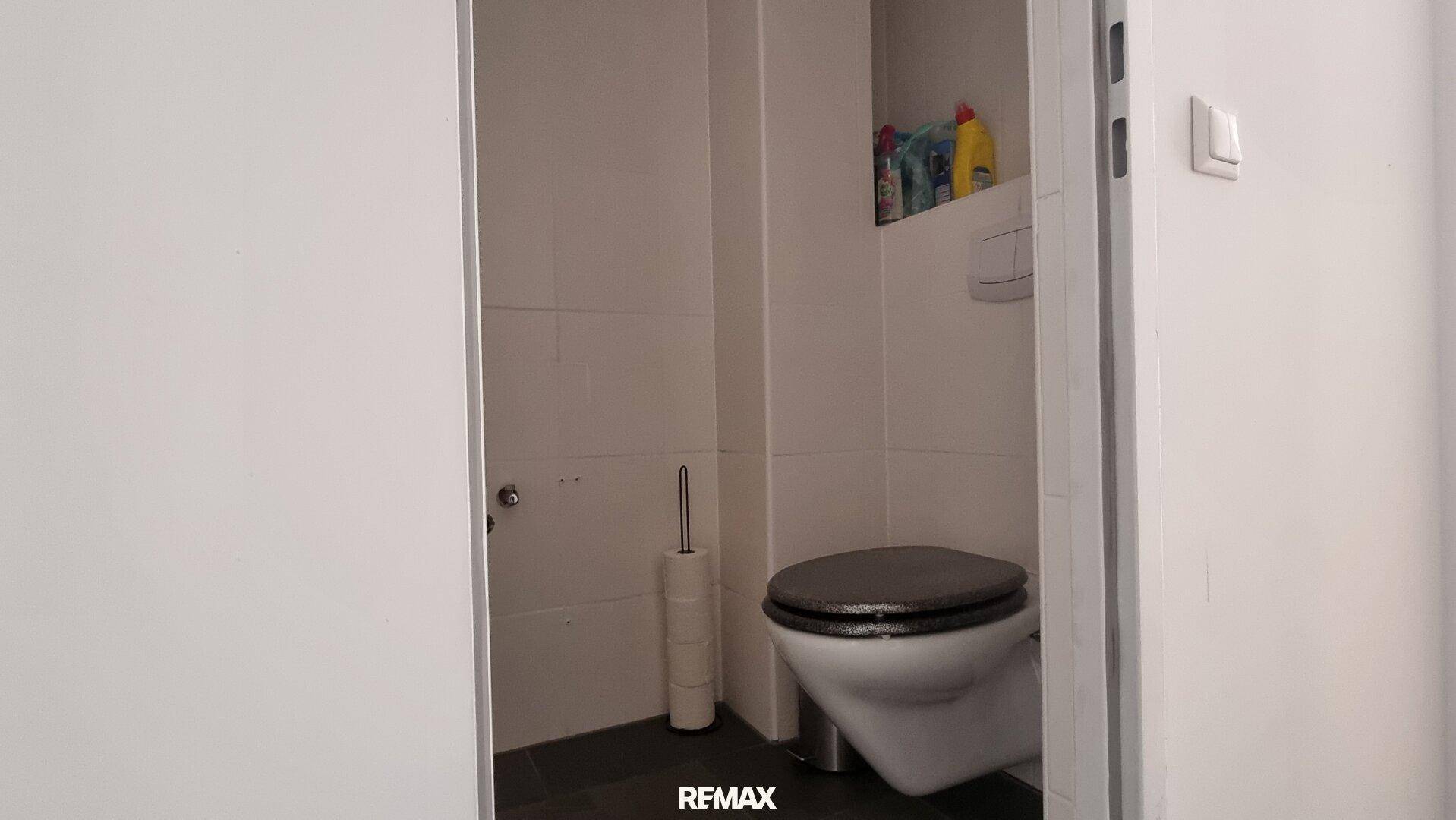 Separates WC mit Wand-WC und dunklen Bodenfliesen.