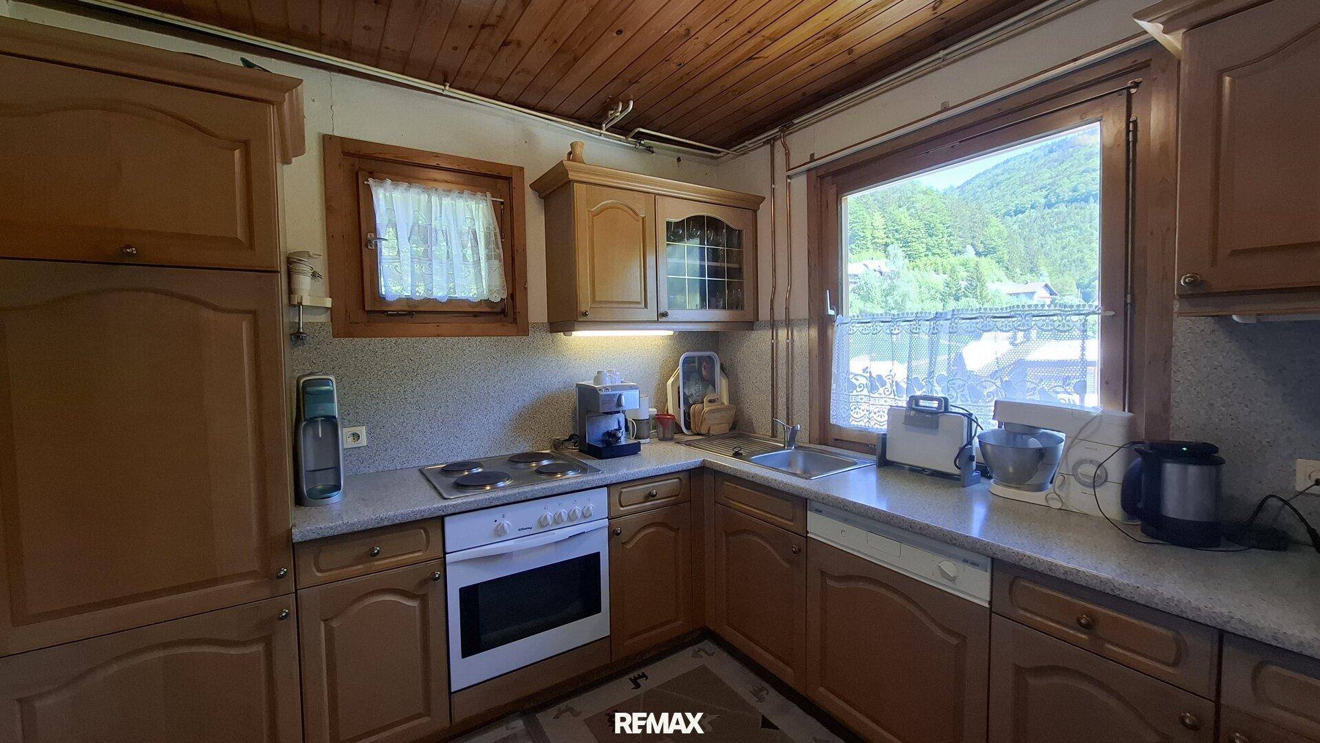 Funktionale Küche mit Holzschränken, Einbaugeräten und Fenster mit Blick ins Grüne.