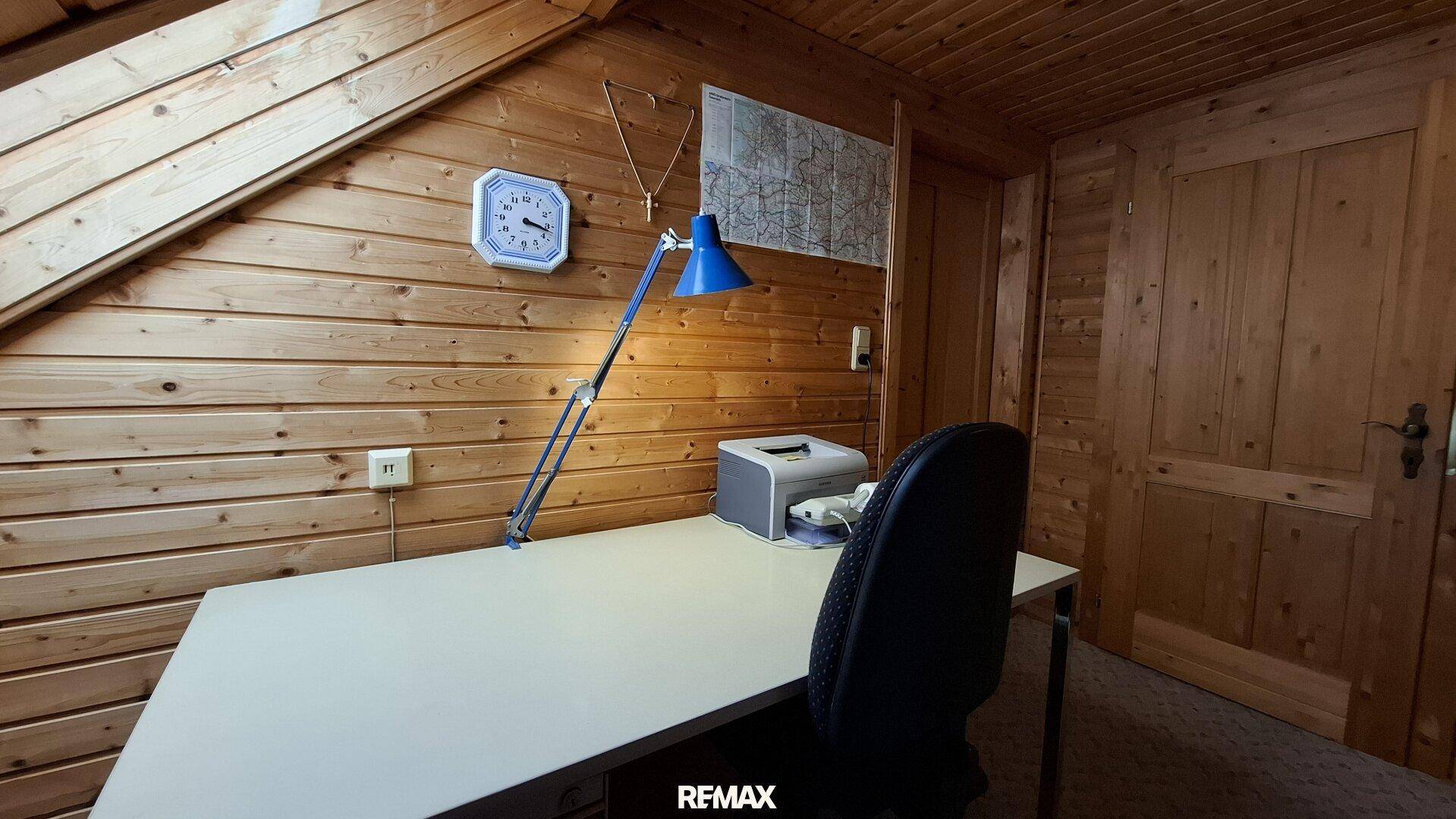 Arbeitszimmer im Dachgeschoss mit Holztäfelung, Schreibtisch und Dachschräge.