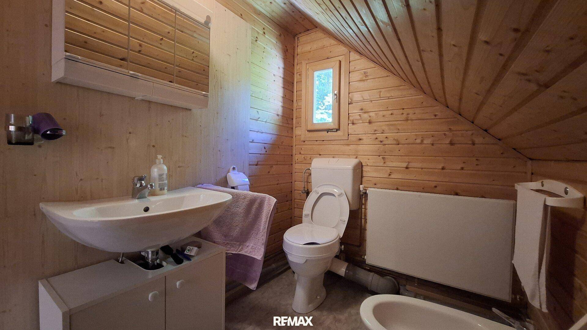 Badezimmer im Dachgeschoss mit Waschbecken, WC, Bidet und Holztäfelung.
