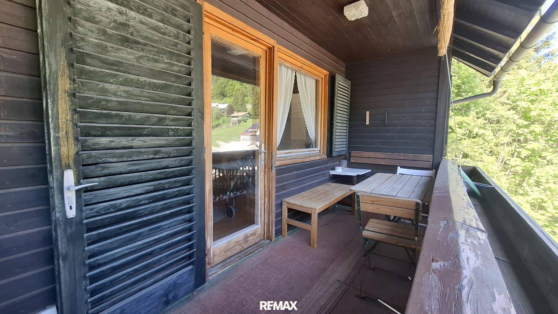 Holzbalkon mit Sitzgelegenheiten und traditionellen Fensterläden, umgeben von Natur.