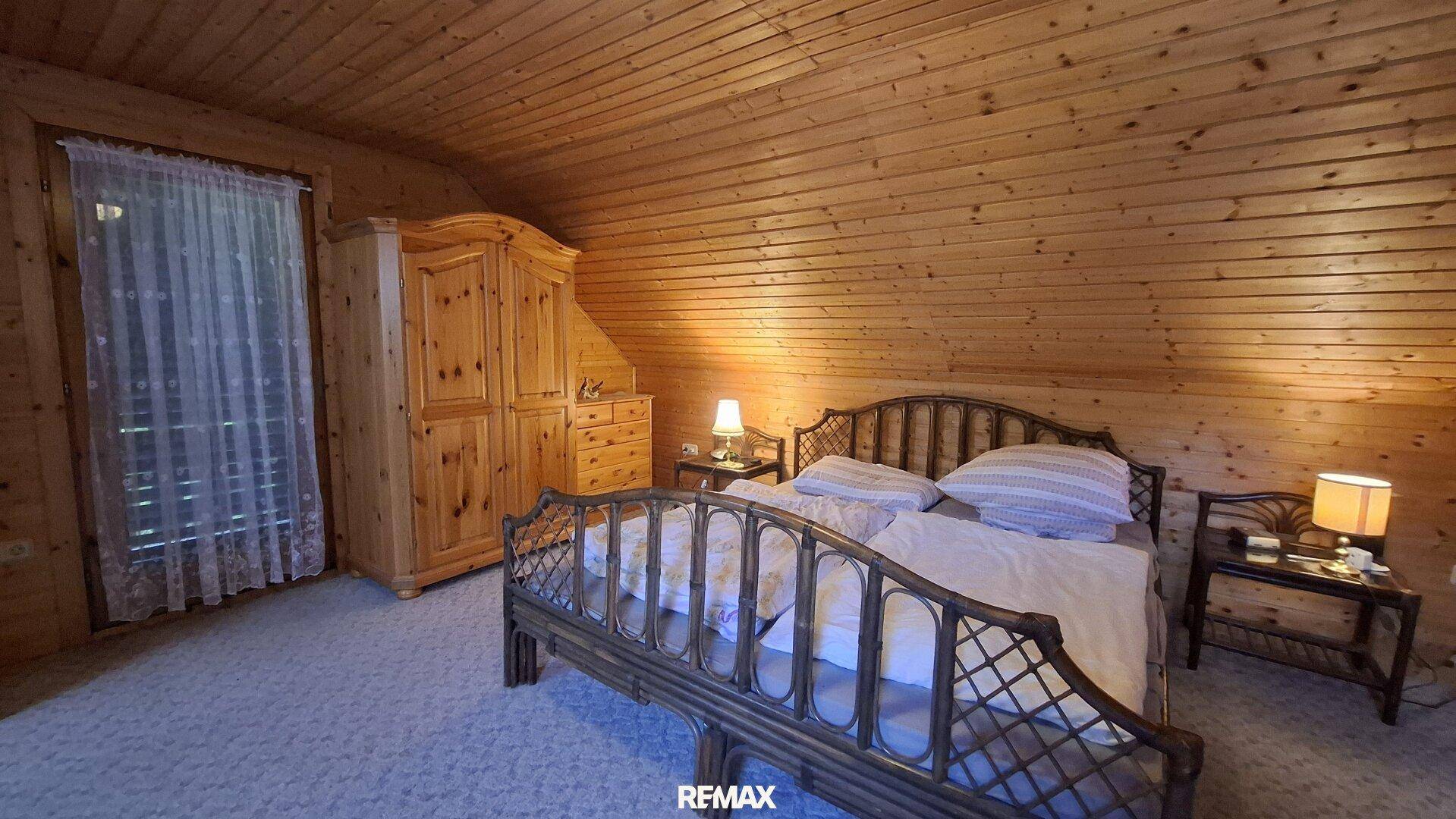 Schlafzimmer im Dachgeschoss mit Holztäfelung, Teppichboden und gemütlichem Bett.