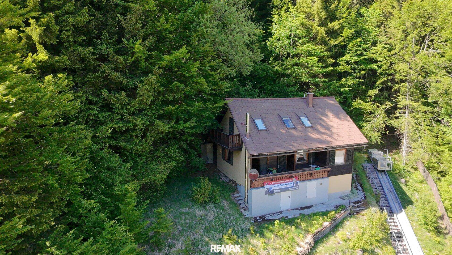 Panoramablick auf das Haus, eingebettet in die grüne Hügellandschaft mit Wald.