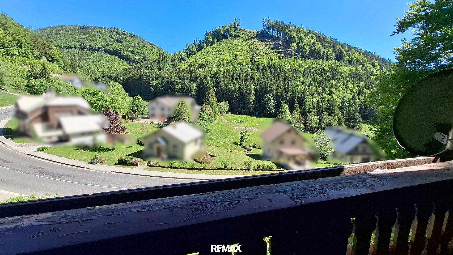 Blick vom Balkon auf die umliegende Berglandschaft und eine Landstraße.