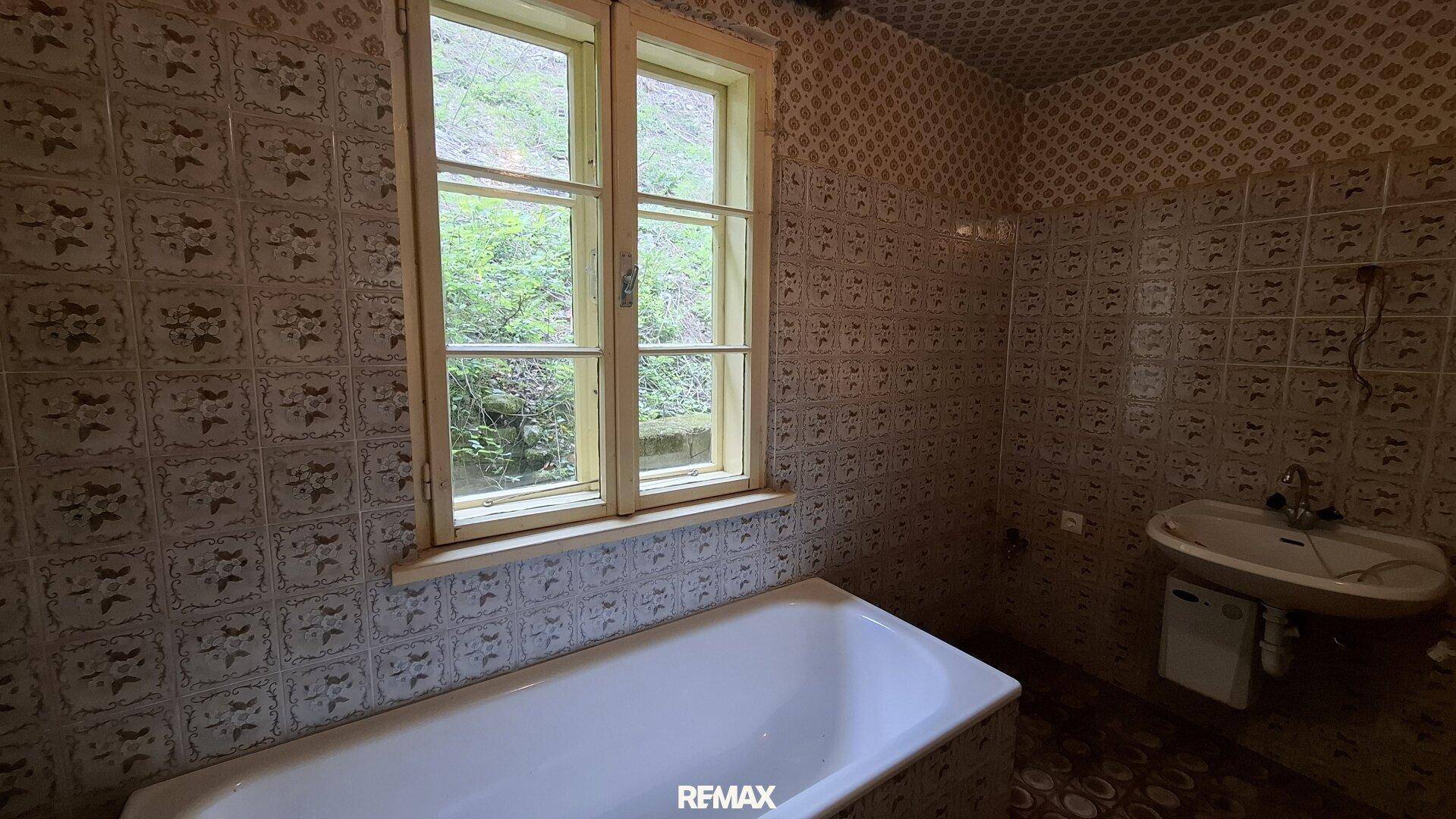 Badezimmer mit Badewanne, Waschbecken und gemusterten Fliesen an Wänden und Boden.
