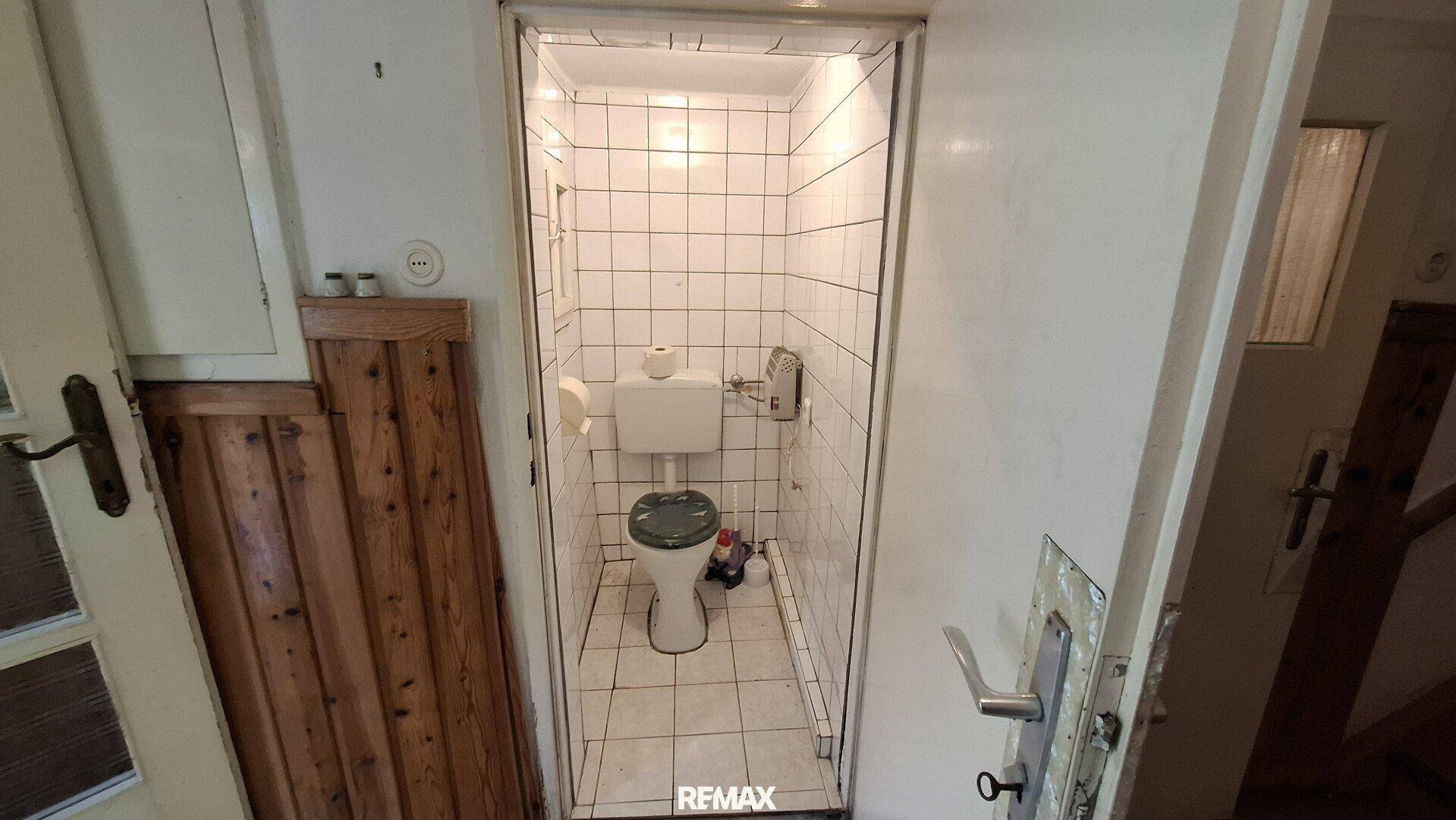 Kleines separates WC mit weißen Fliesen und einfacher Toilette.
