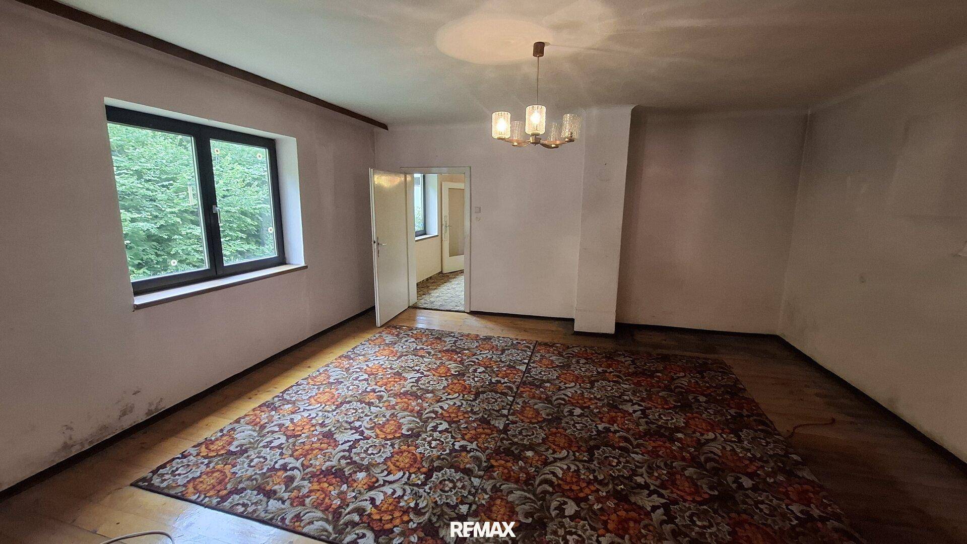 Geräumiges Wohnzimmer mit großem Teppich, Holzboden und Blick ins Grüne.