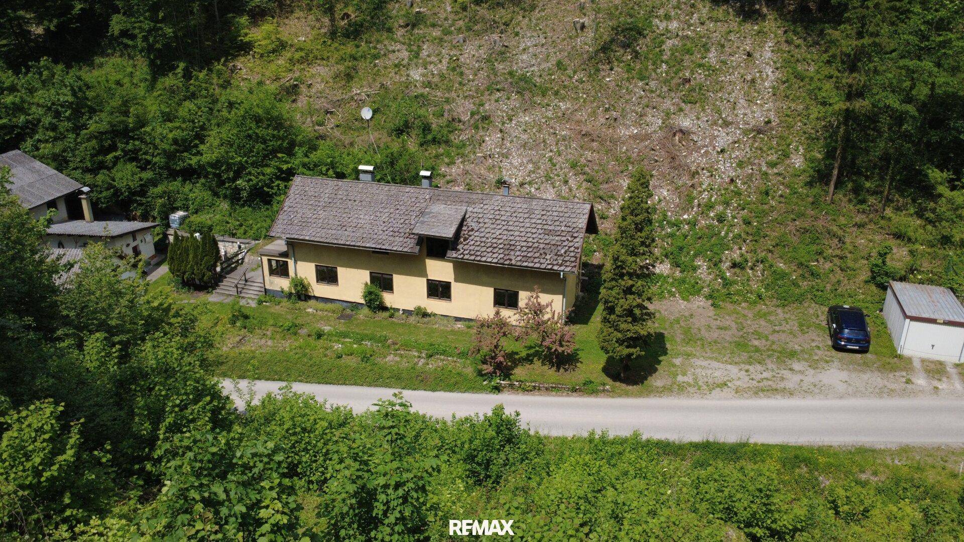 Luftaufnahme eines Hauses in grüner, bewaldeter Landschaft mit Zufahrtsstraße.