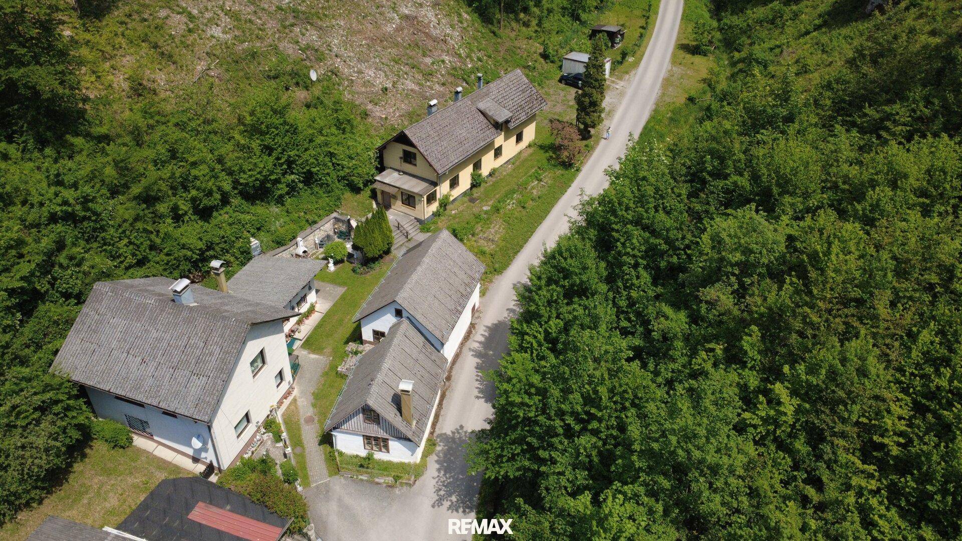 Luftaufnahme von mehreren Häusern in einer grünen, ländlichen Umgebung mit kurvenreicher Straße.