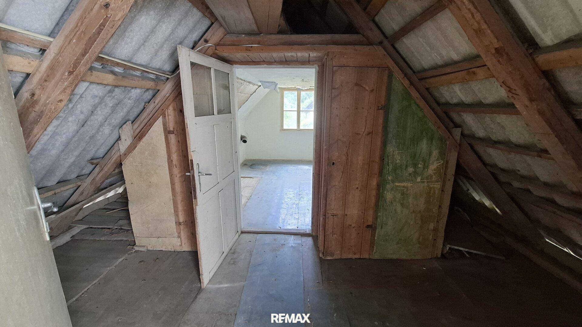 Dachboden mit sichtbaren Holzbalken und Zugang zu einem weiteren Raum.