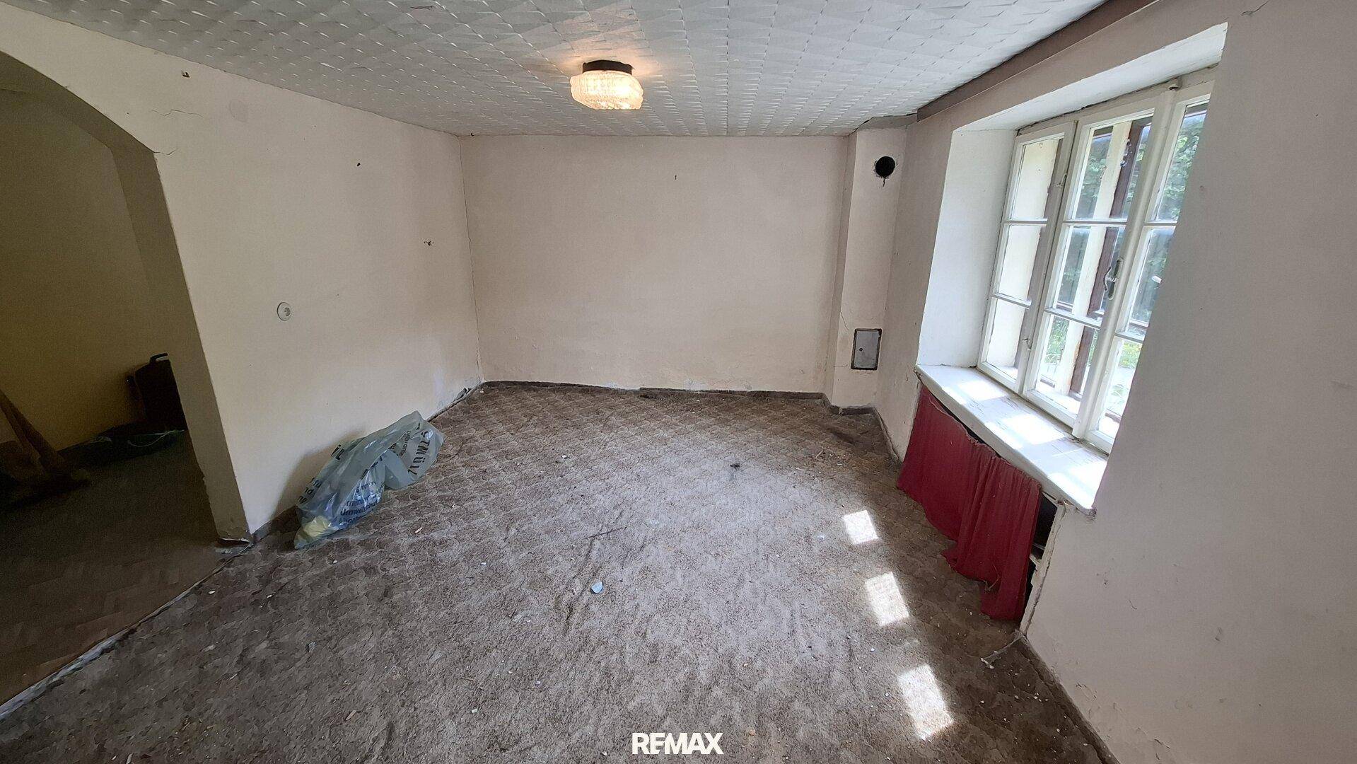 Unaufgeräumtes Zimmer mit Teppichboden, Fenster und einfacher Beleuchtung.