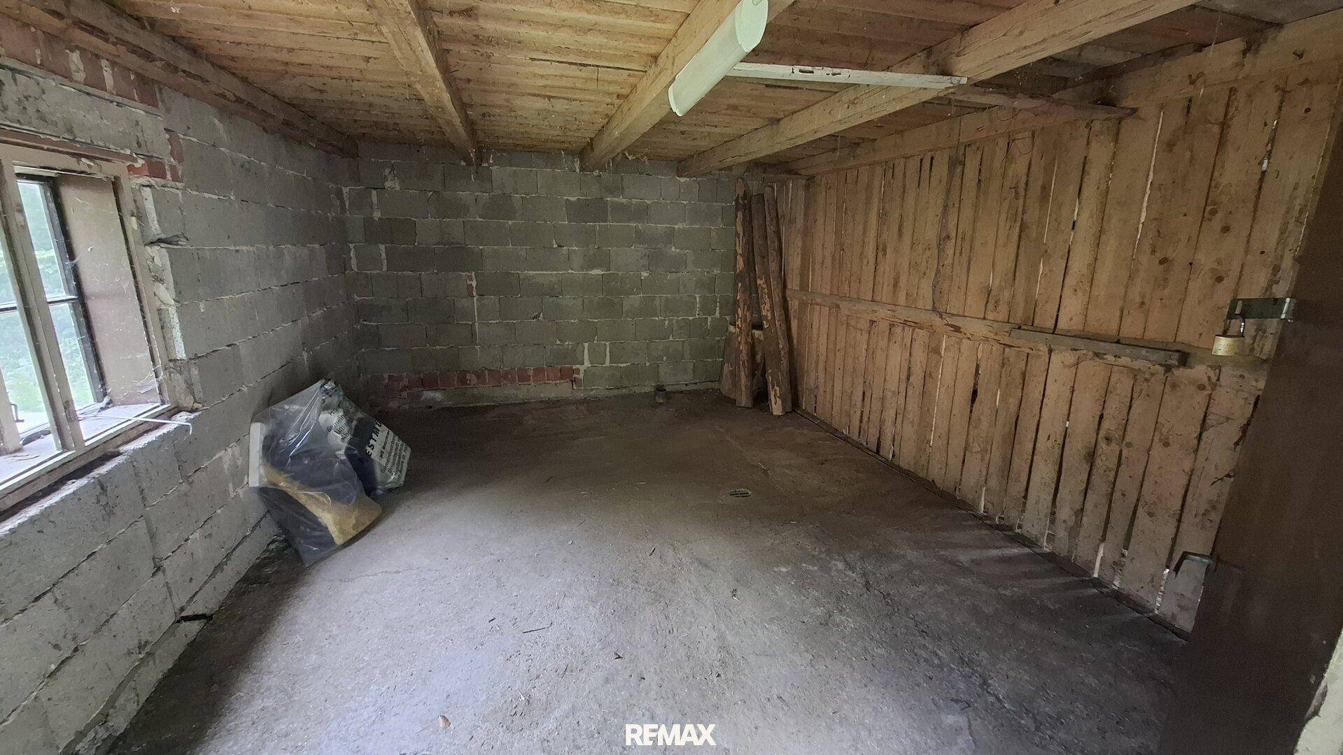 Geräumige Garage mit Betonboden, Ziegelwänden und Holzdecke, ideal als Werkstatt.