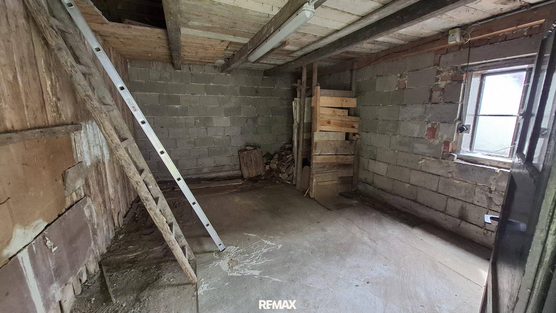 Unfertiger Kellerraum mit Betonwänden, Holzdecke und kleinem Fenster, bereit für Ausbau.