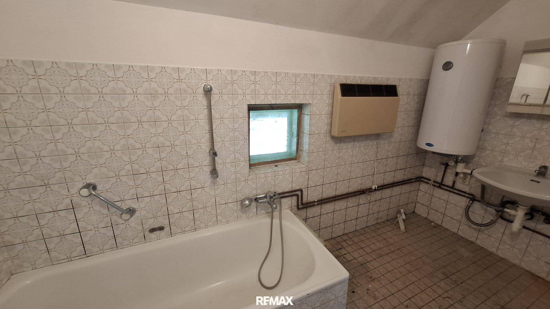Badezimmer mit Badewanne, Waschbecken, Boiler und kleinen Fliesen an den Wänden.