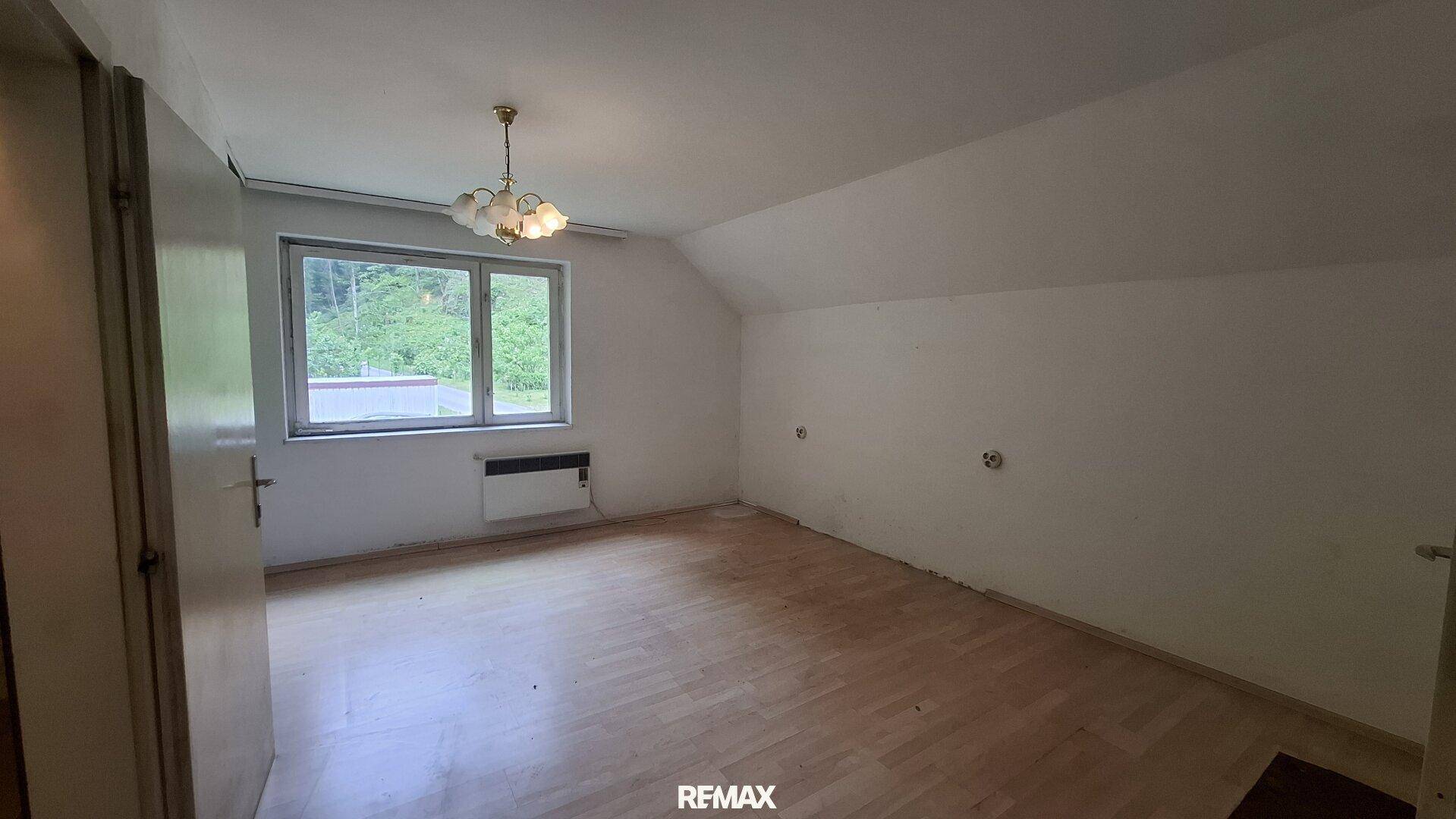 Leeres Schlafzimmer mit Dachschräge, Laminatboden und Blick ins Grüne.