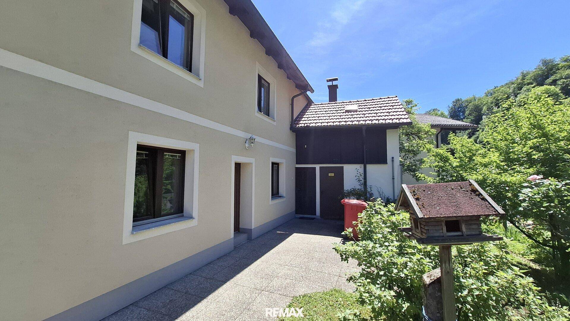 Seitenansicht des Hauses mit heller Fassade, braunen Fenstern und einem kleinen Gartenweg.