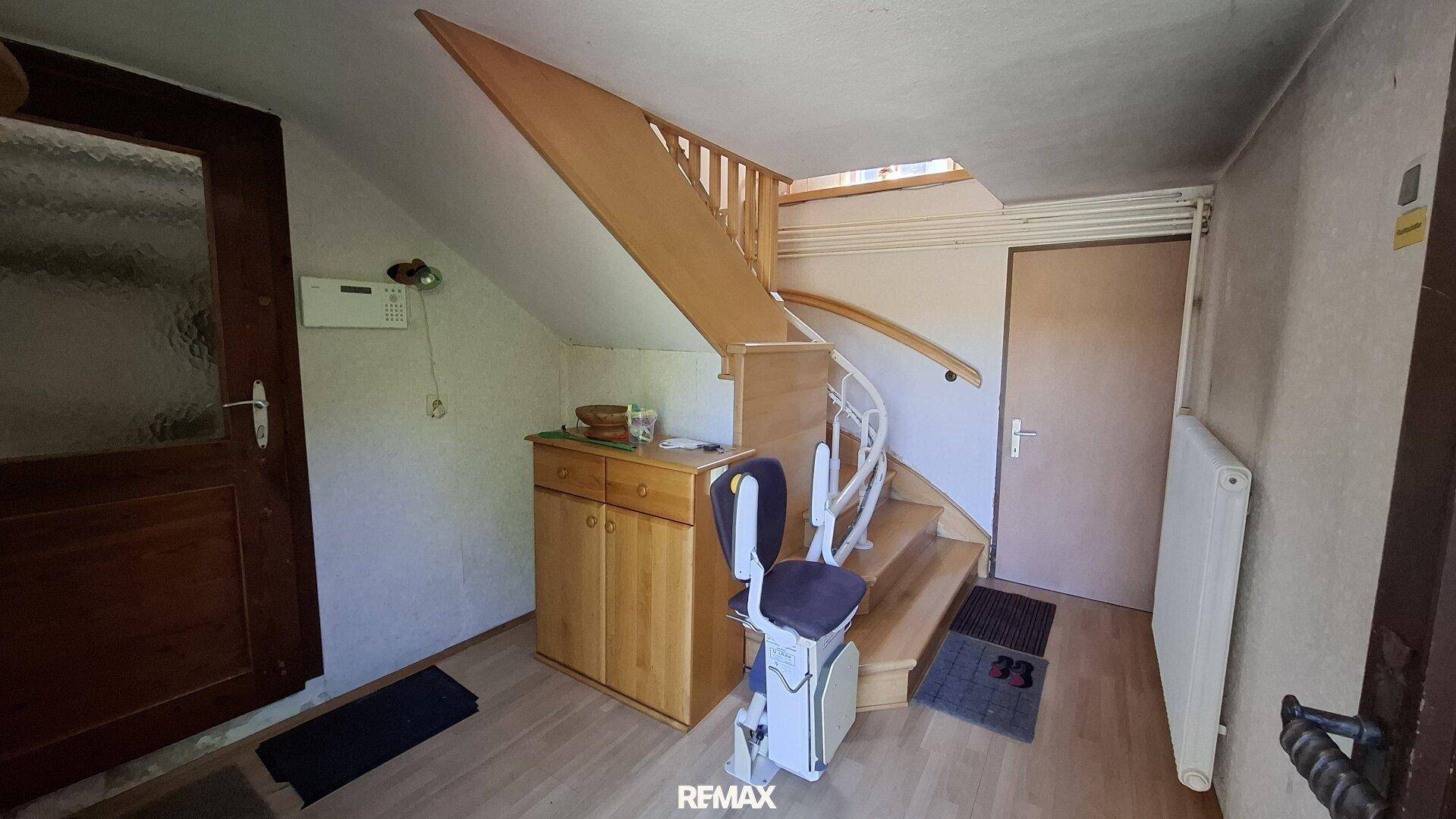 Treppenhaus mit Holztreppe, Treppenlift und einem kleinen Holzschrank.