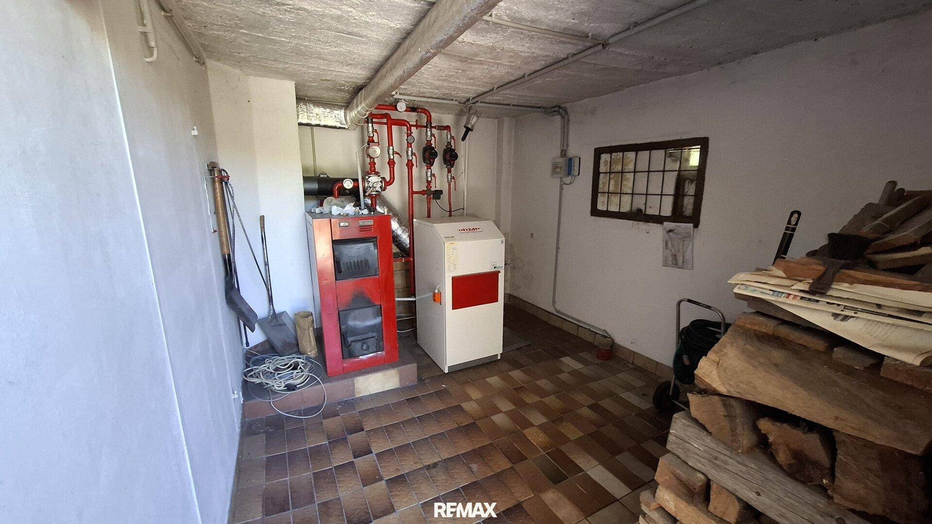 Heizraum mit Heizungsanlage und gestapeltem Brennholz auf Fliesenboden.