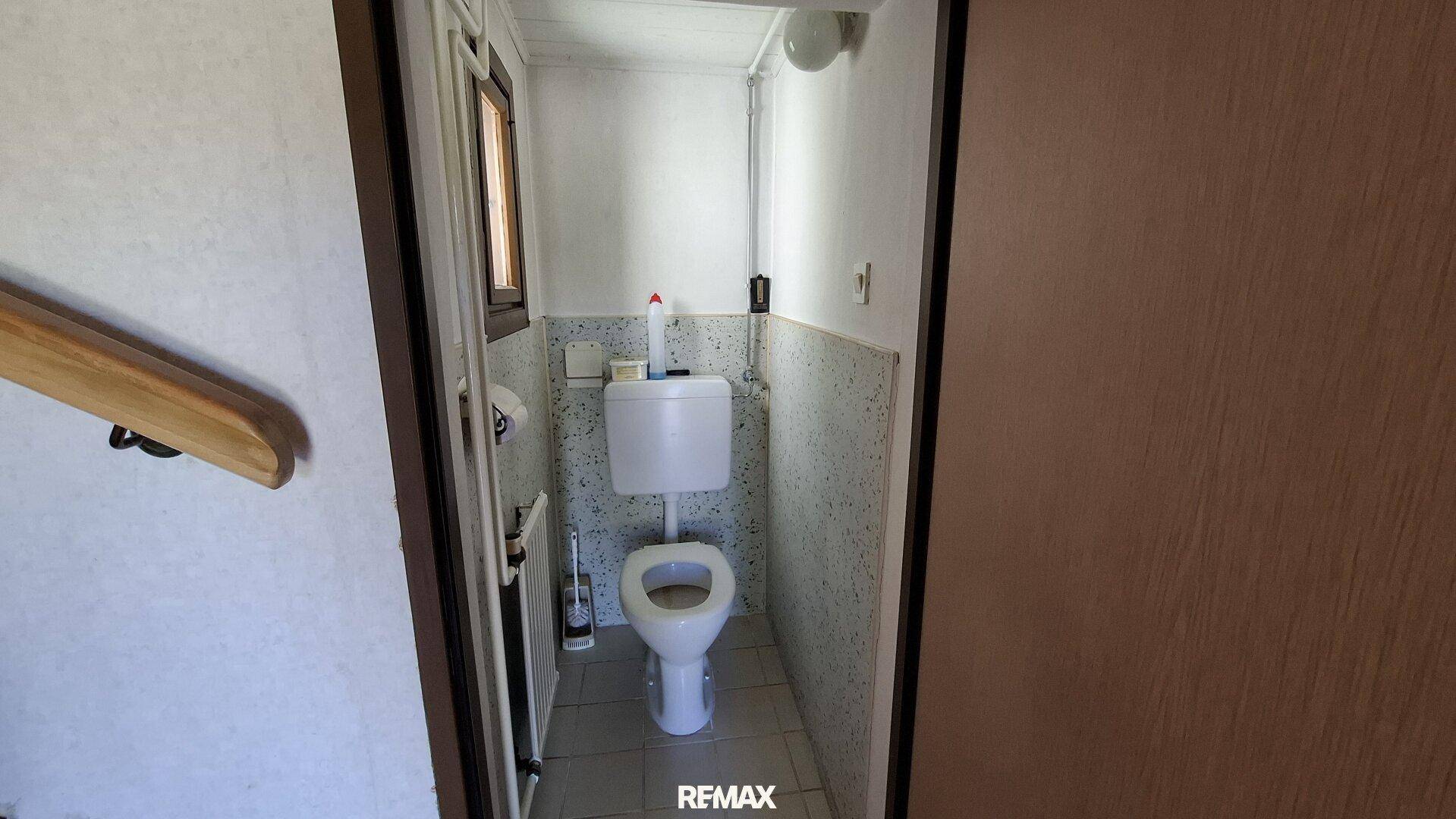 Kleines WC mit Toilette, Fliesenboden und einem Fenster für natürliche Belüftung.