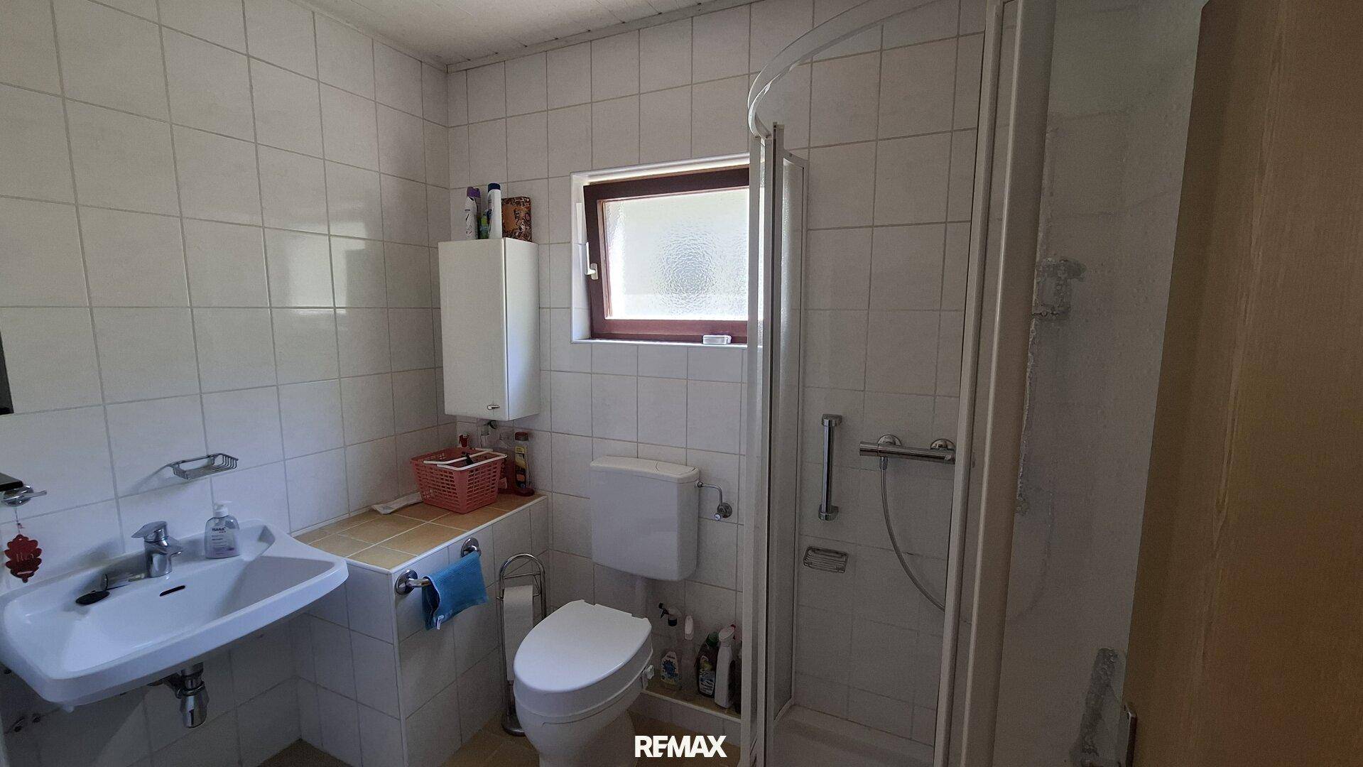 Badezimmer mit Dusche, Toilette, Waschbecken und vollständig gefliesten Wänden.